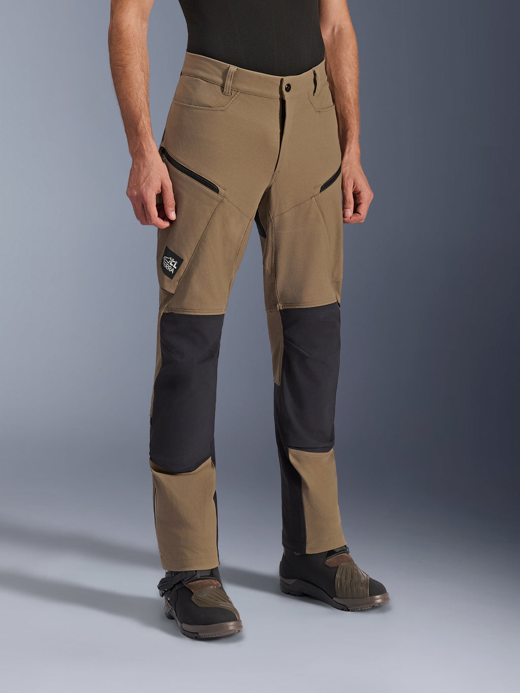 Alpinestars Flex-AST Explorer Hose, Adventure-Motorradhose in Walnut Black, hellbraunes Textil mit schwarzen verstärkten Knie- und Gesäßpartien, Cargotaschen mit Reißverschluss und All Terra Logo-Patch, getragen mit technischen Motorradstiefeln.