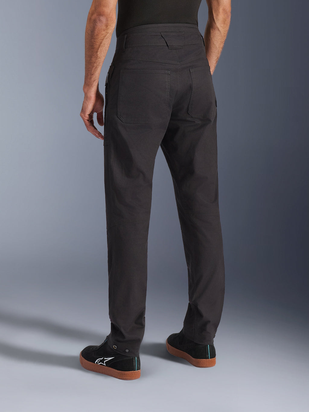 Alpinestars Flex-AST Canvas Broek, zwart, achteraanzicht met erfgoed werkkleding-ontwerp en grote achterzakken, ergonomische urban rijpasvorm, gedragen met zwarte Alpinestars sneakers.