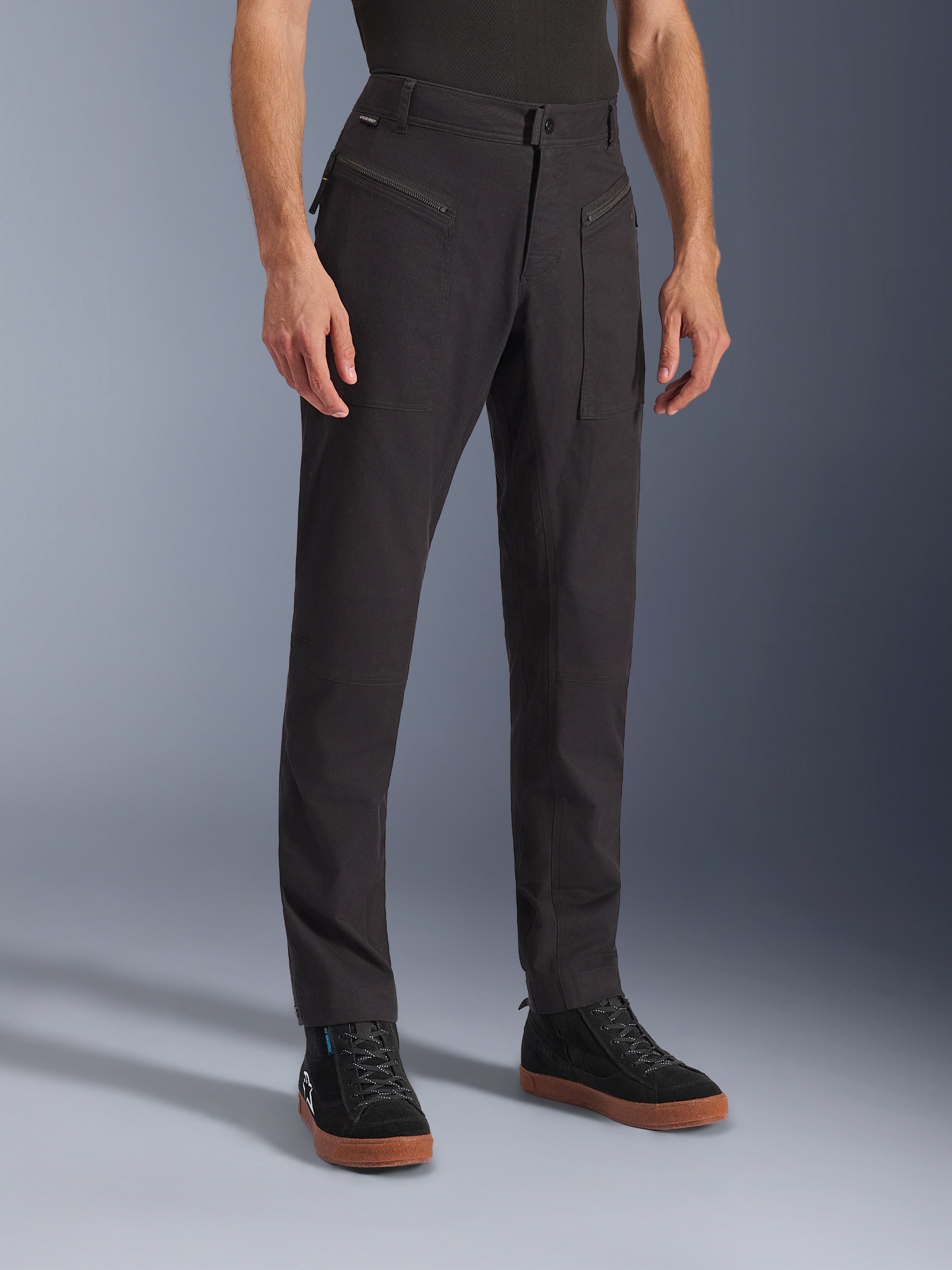 Alpinestars Flex-AST Canvas broek, zwart, urban motorbroek, gedragen door model met zwarte sneakers, met een heritage workwear design, stretch polykatoen twill stof en functionele ritszakken aan de voorzijde.