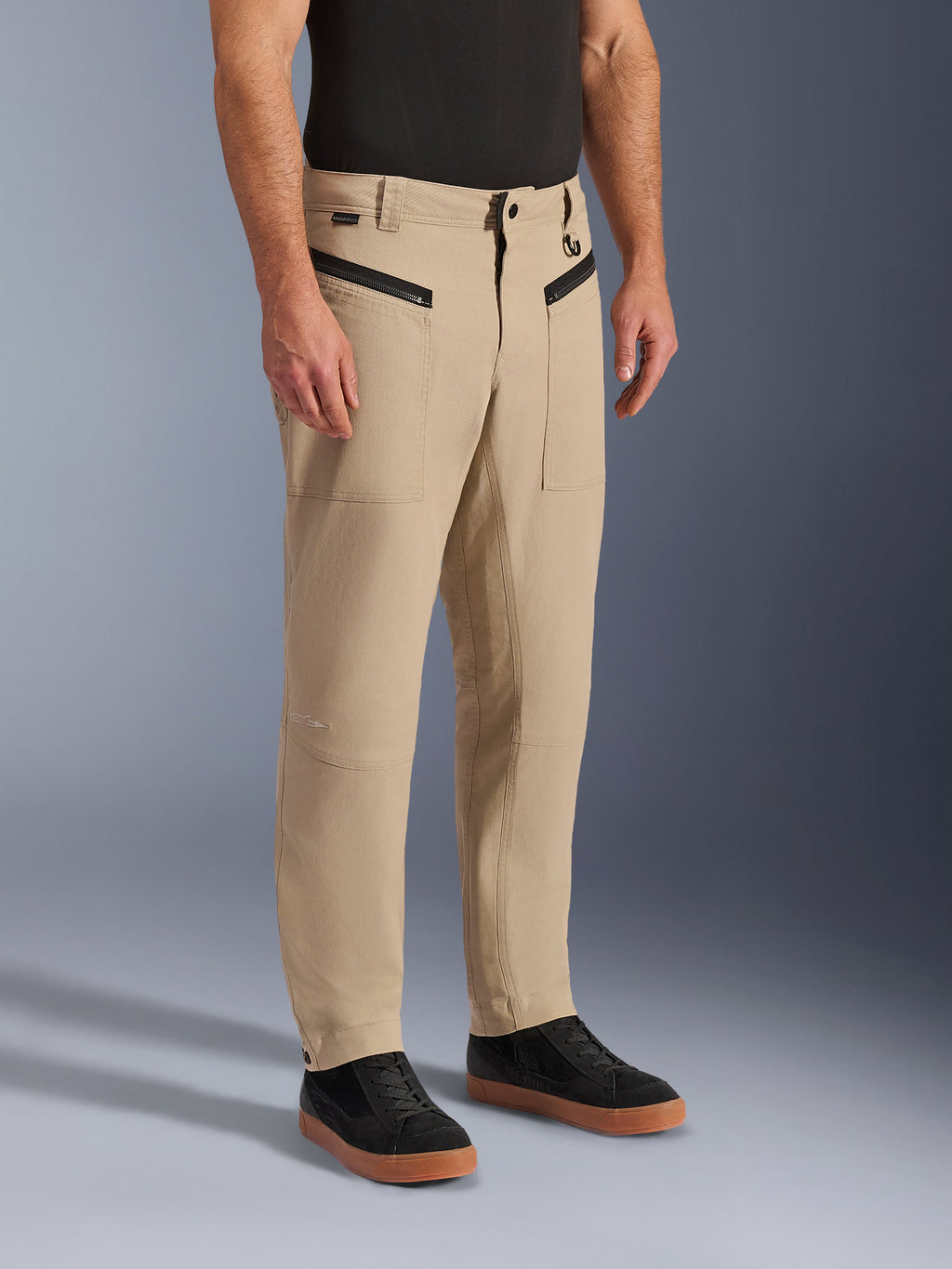 Alpinestars Flex-AST Canvas Hose, urbane Motorradhose, Hellbraun, mit Heritage-Workwear-Styling, vorderen Reißverschlusstaschen und ergonomischen Knieeinsätzen, kombiniert mit schwarzen Sneakern und einem schwarzen T-Shirt, moderne urbane Fahrausrüstung