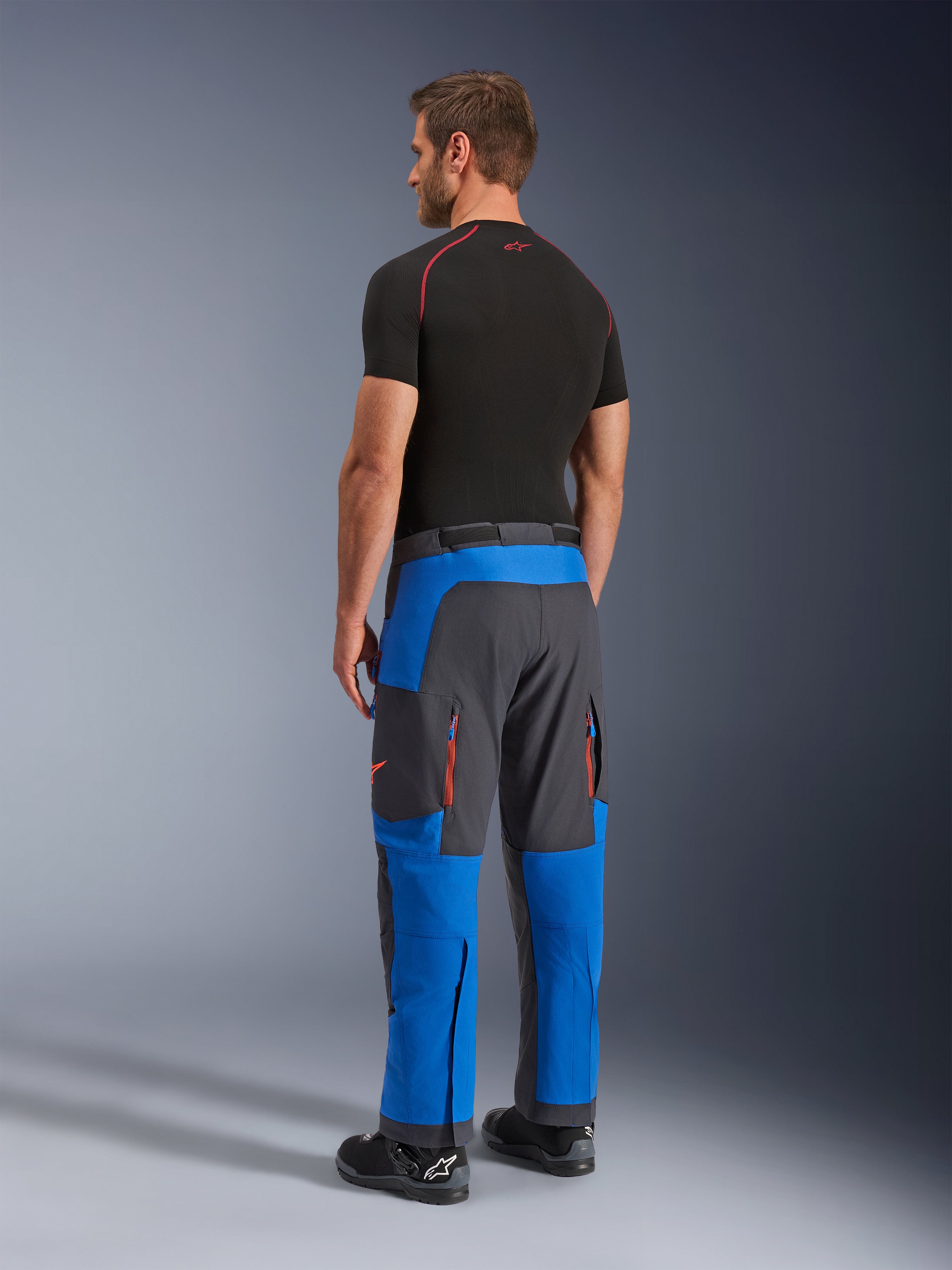 Pantalon Alpinestars Maxdura Dual, pantalon de moto d'aventure, bleu royal et gris foncé, vue de dos porté par un mannequin, doté d'aérations zippées orange, coupe aventure par-dessus la botte et textile extensible durable.