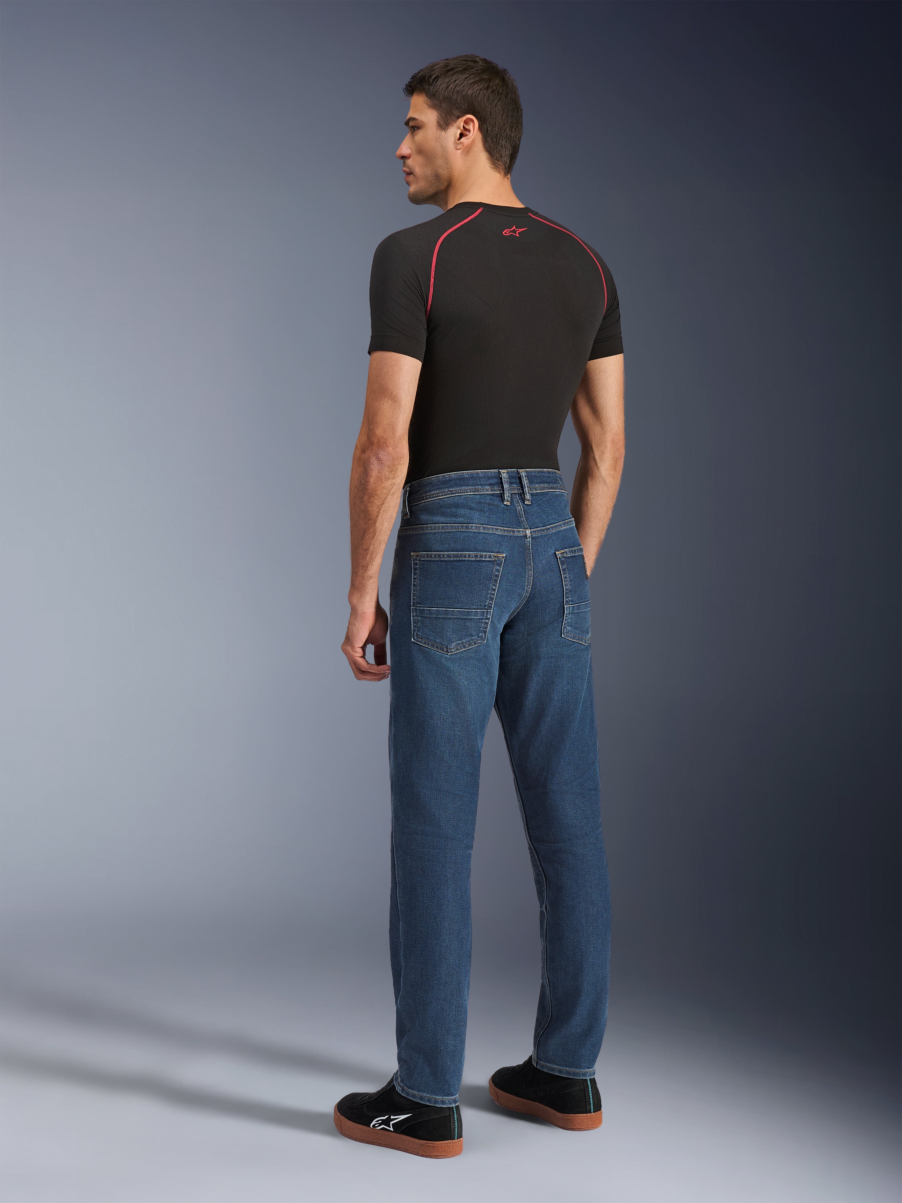 Alpinestars Flex-AST 5 Denim broek, Indigo Washed, achteraanzicht van model dat de broek draagt, urban motorjeans, toelopende pasvorm met monolayer stretchdenim, gecombineerd met een zwart T-shirt en zwarte sneakers