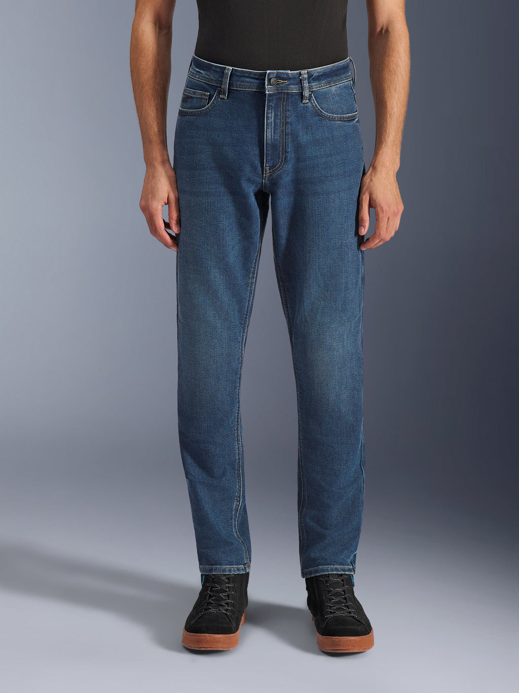 Alpinestars Flex-AST 5 Denim Broek, urban motorjeans, Indigo Washed blauw, vooraanzicht met een moderne toelopende pasvorm en casual five-pocket styling, gedragen met een zwarte top en sneakers, ontworpen voor stedelijk rijcomfort en bescherming.