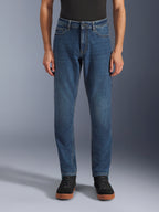 Alpinestars Flex-AST 5 Denim Broek, urban motorjeans, Indigo Washed blauw, vooraanzicht met een moderne toelopende pasvorm en casual five-pocket styling, gedragen met een zwarte top en sneakers, ontworpen voor stedelijk rijcomfort en bescherming.