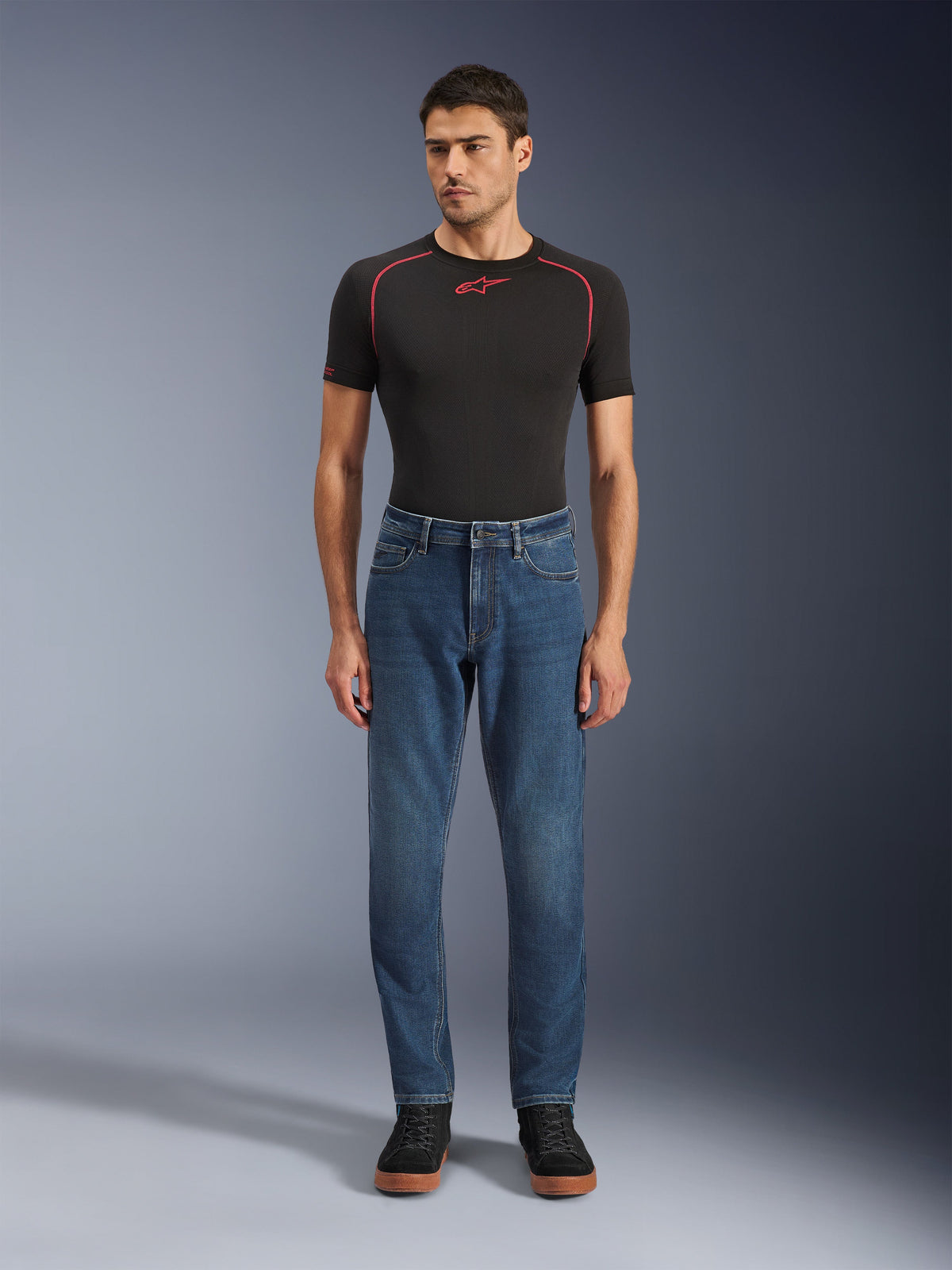 Alpinestars Flex-AST 5 Denim-Hose, Motorrad-Jeanshose, Indigo Washed, getragen mit schwarzem Performance-T-Shirt und schwarzen Sneakern, mit schmal zulaufender Passform und Monolayer-Stretch-Denim-Konstruktion für urbane Fahrten