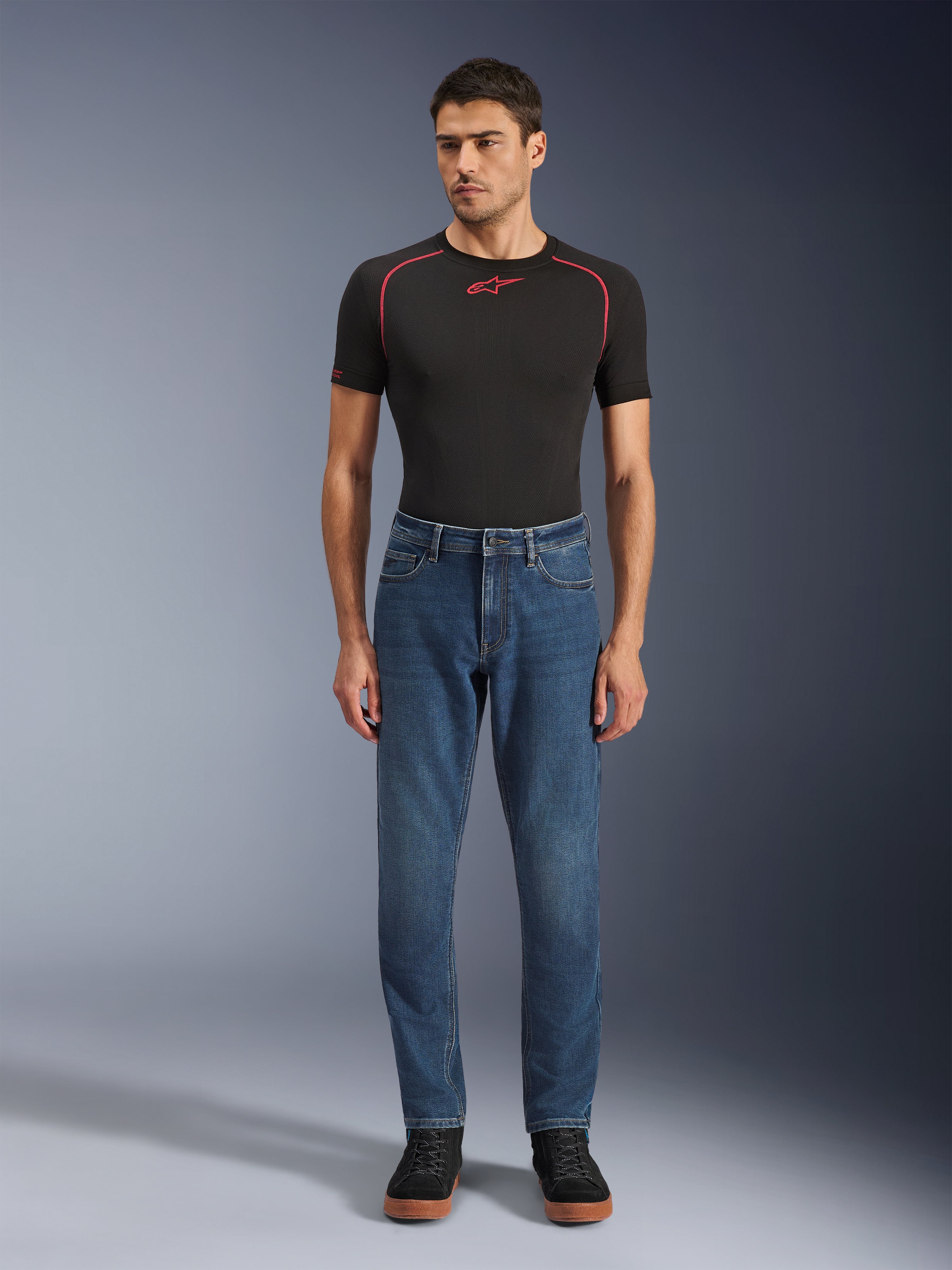 Alpinestars Flex-AST 5 Denim Broek, Indigo Washed blauwe denim motorbroek, regular tapered fit, gedragen door een model met een zwarte Alpinestars basislaag en zwarte vrijetijdsschoenen, urban riding lifestyle kleding