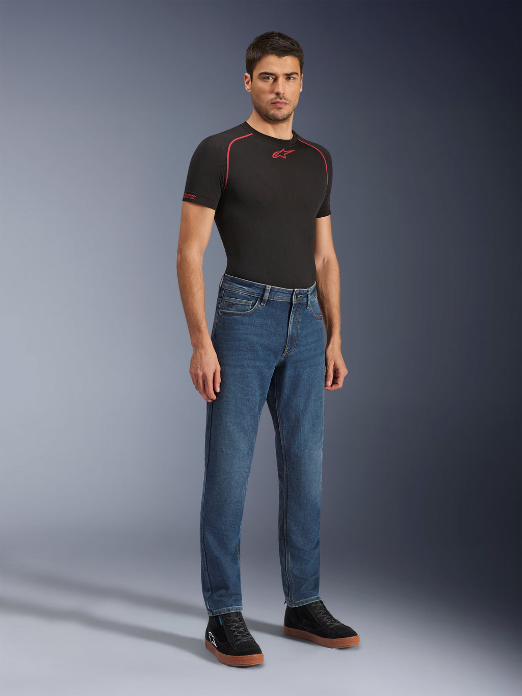 Alpinestars Flex-AST 5 Denim broek, Indigo Washed motorjeans, moderne toelopende pasvorm, gedragen door een mannelijk model met een zwart performance t-shirt en zwarte sneakers, casual stedelijke motorkleding