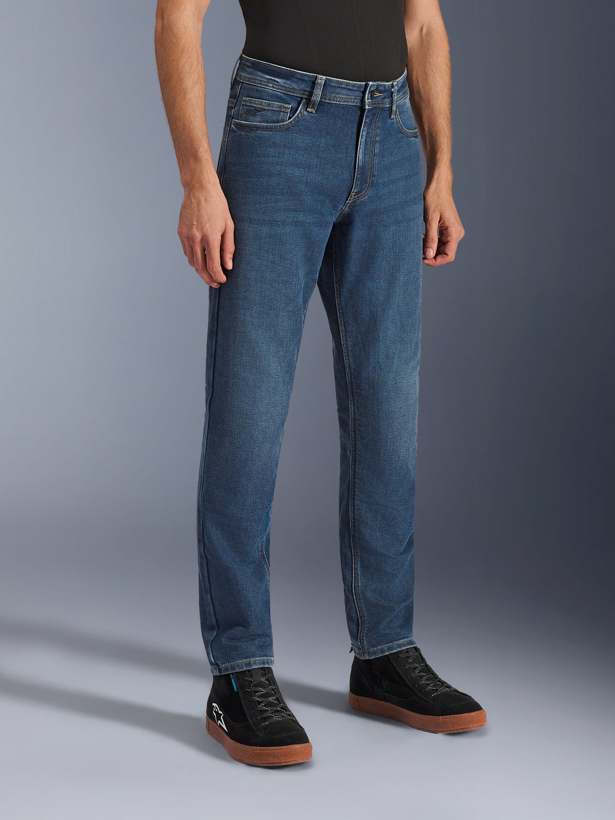 Alpinestars Flex-AST 5 Denim Pants, Indigo Washed motorjeans, regular tapered fit, gedragen met zwarte high-top sneakers en een zwart shirt, casual urban motorkleding met een klassieke denim uitstraling.