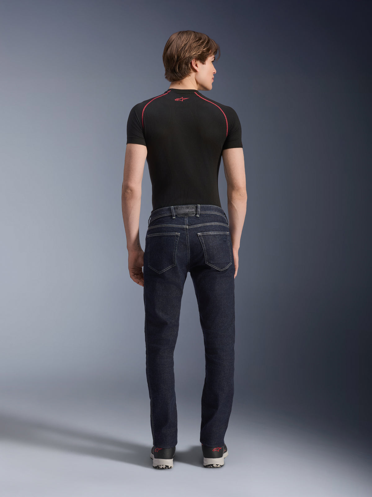 Alpinestars Copper V3 Denim Pants in Rinse Blue, urban motorjeans vanaf de achterkant gezien, met een rechte pijp, regular fit en achterzakken, gedragen met een zwart shirt met korte mouwen en sneakers.