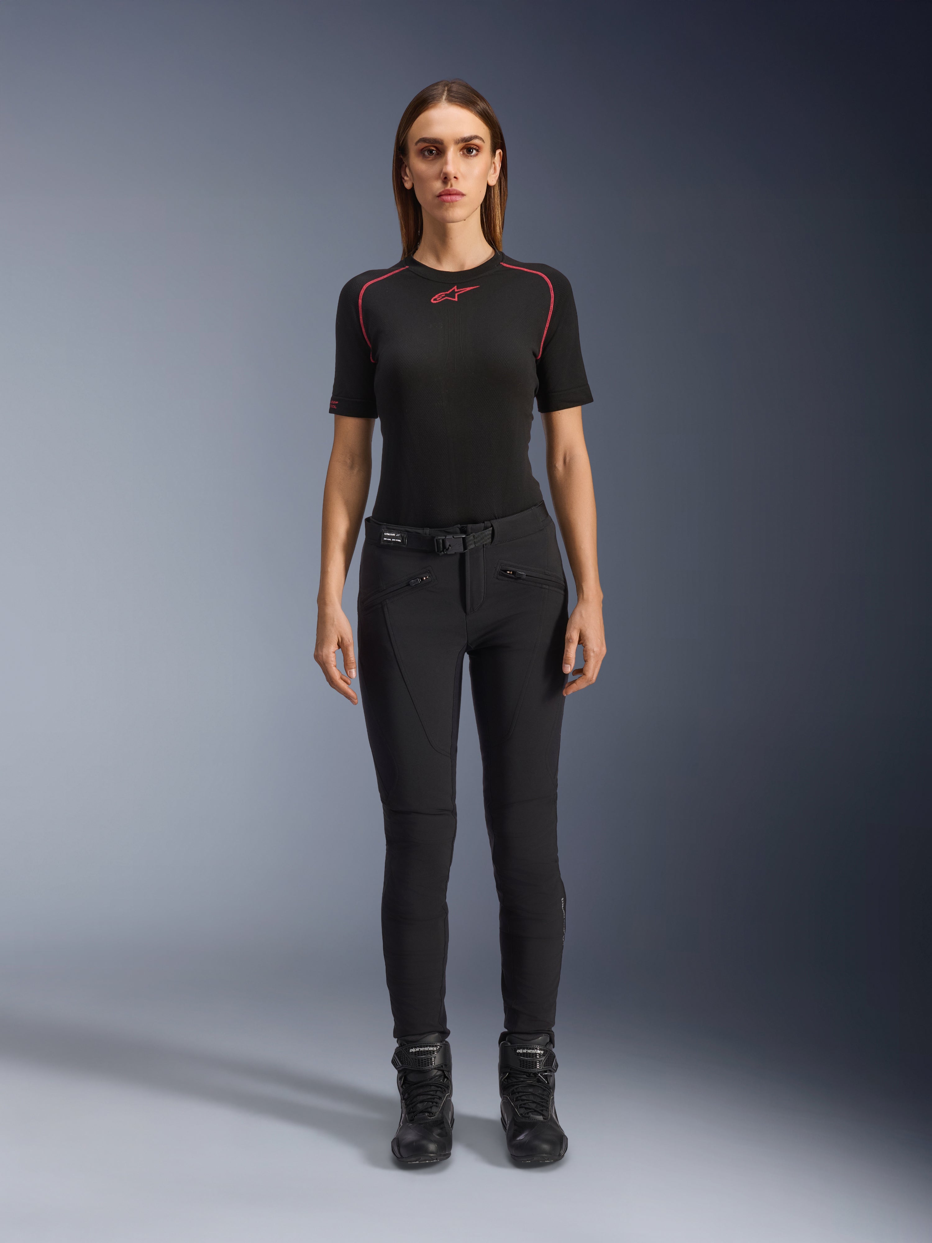 Alpinestars Alamosa damesbroek, slim-fit zwarte motorbroek, getoond op een model van voren, met ritszakken aan de voorkant en een geïntegreerde tailleriem, minimalistische op streetwear geïnspireerde stijl voor stedelijk rijden
