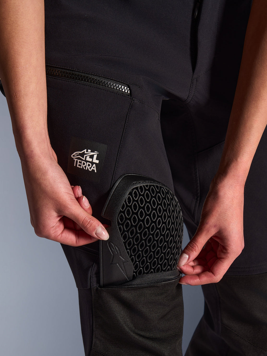 Gros plan du pantalon Alpinestars Stella Flex-AST Explorer en noir, montrant la poche de protection externe utilisée pour insérer la protection de genou Nucleon Flex Plus, détail de la protection avec motif en nid d'abeille, logo « ALL TERRA » sur la cuisse, équipement d'aventure technique en textile pour femme