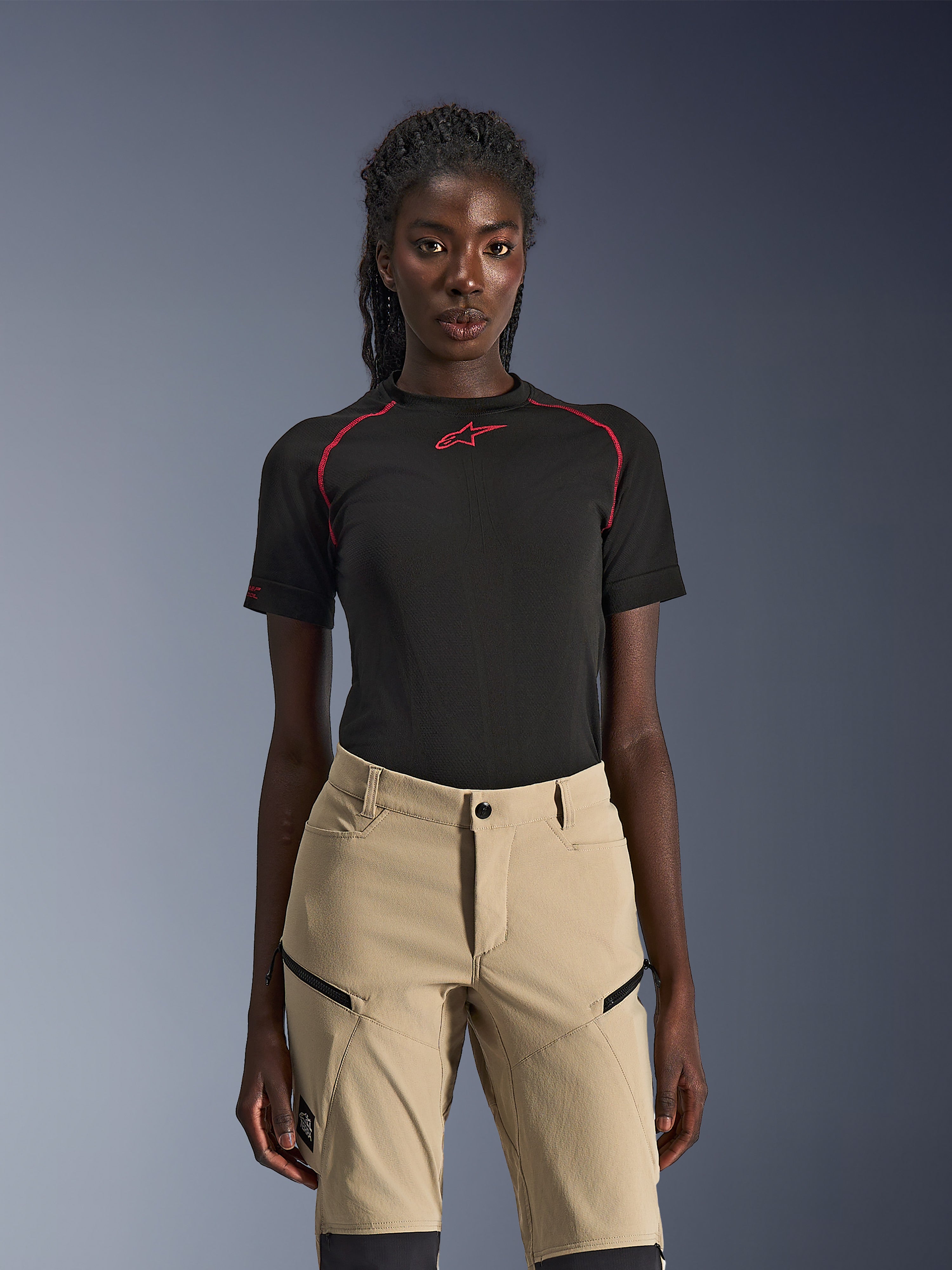Alpinestars Stella Flex-AST Explorer Pants, Women's motorcycle pants in Sand, worn with a black technical short-sleeve top with red stitching, adventure touring gear featuring zippered cargo pockets and durable ripstop fabric.