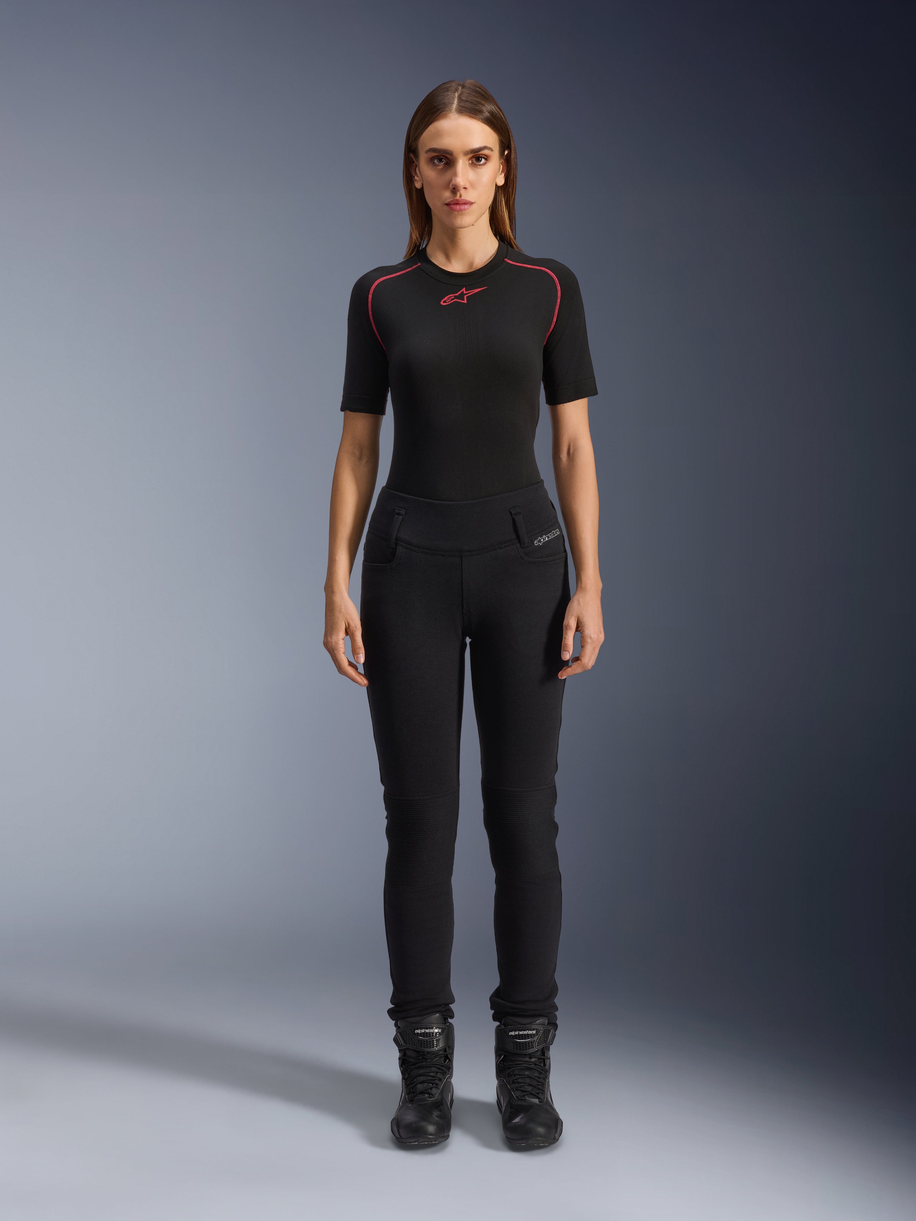 Alpinestars Banshee dameslegging, zwarte motorlegging, nauwsluitende anatomische pasvorm, gedragen door een vrouwelijk model met een zwarte basislaag en motorlaarzen, voorzien van geribbelde kniepanelen en een hoge taille voor urban rijden.