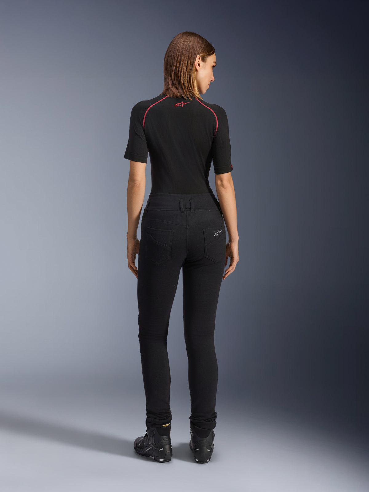 Leggings Banshee Femme Alpinestars, leggings de moto noirs, vue arrière montrant la coupe moulante et le tissu extensible anatomique, avec poches arrière et détail du logo, portés avec une couche de base noire et des chaussures de moto, équipement de moto urbain pour femme