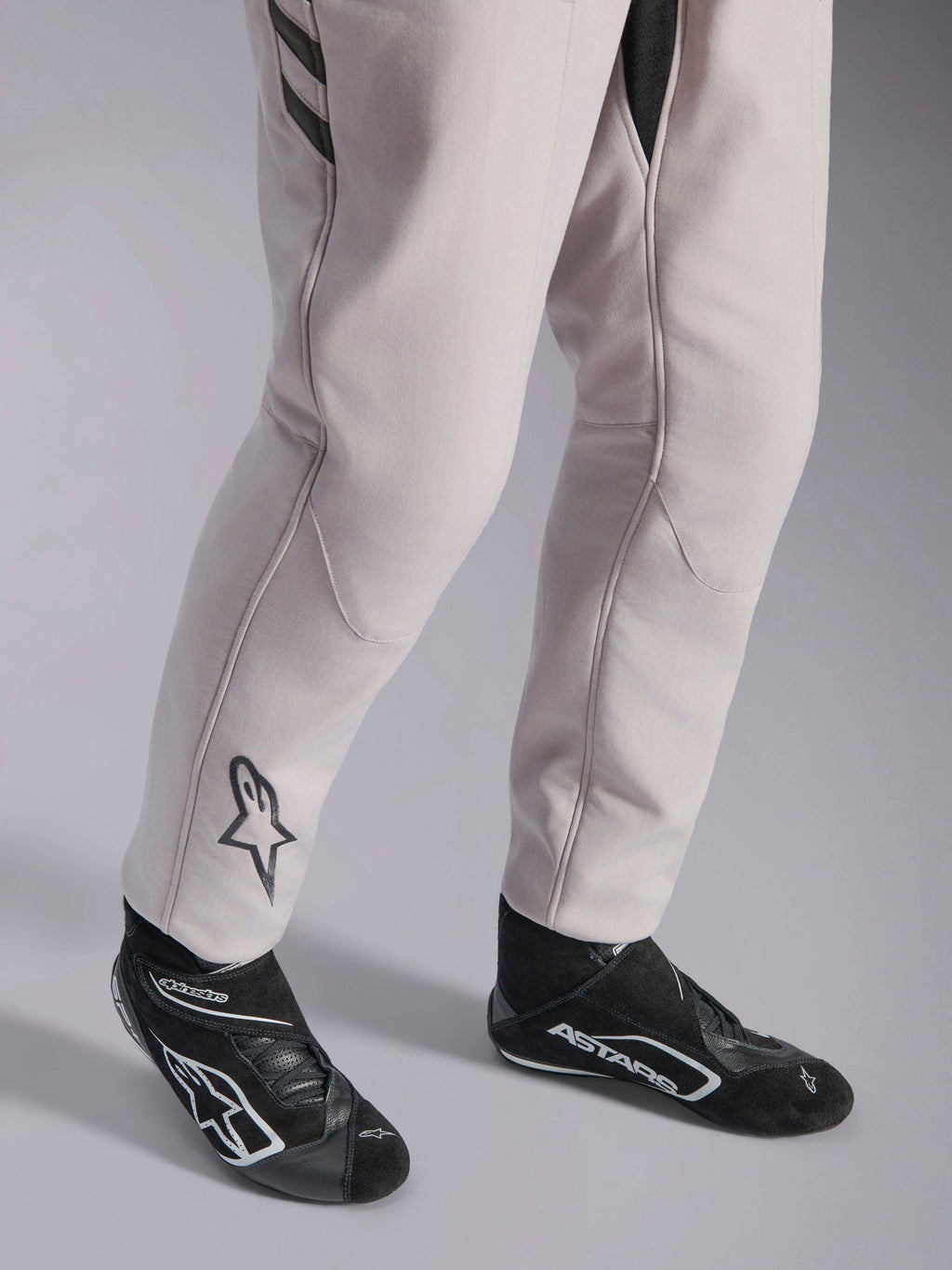 Alpinestars GP Race V3 Suit FIA, combinaison de course automobile Silver Anthracite, vue détaillée du bas des jambes et des bottines de course noires, avec le logo Astars noir sur le mollet, équipement de sport automobile professionnel avec bords-côtes.
