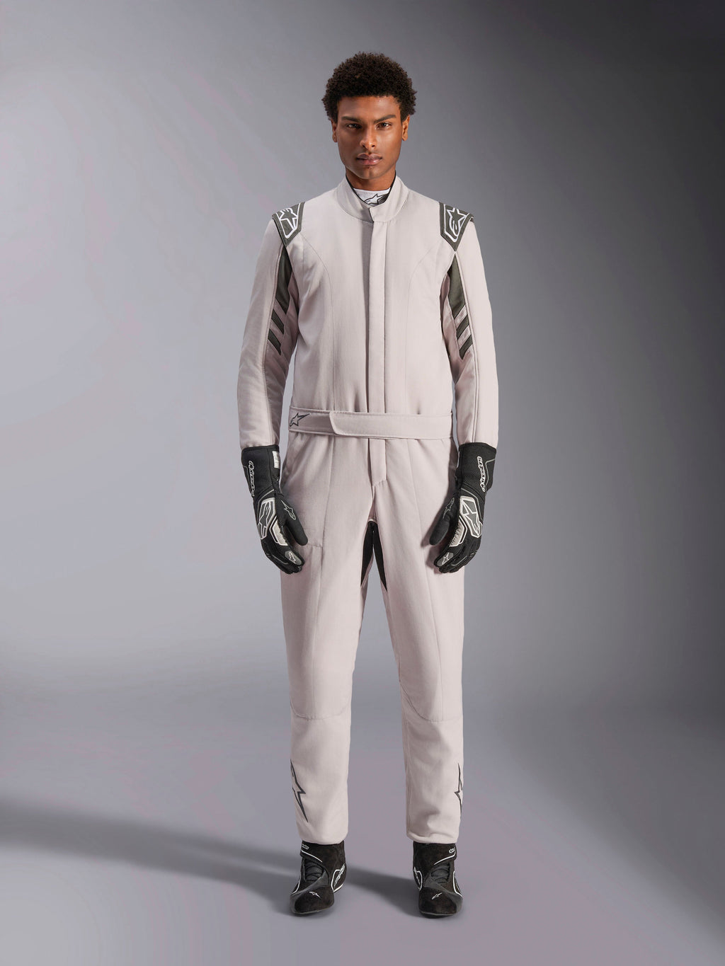 Alpinestars GP Race V3 Suit FIA en Silver Anthracite, combinaison de course automobile une pièce portée par un mannequin, dotée d'épaulettes et de détails gris foncé, accompagnée de gants et de bottines de course noirs, équipement de protection professionnel pour le sport automobile