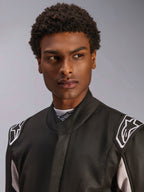 Combinaison Alpinestars GP Race V3 FIA, combinaison de course automobile noire portée par un homme, vue rapprochée montrant le col souple et les logos d'étoiles blancs sur les épaulettes, équipement de protection professionnel pour le sport automobile