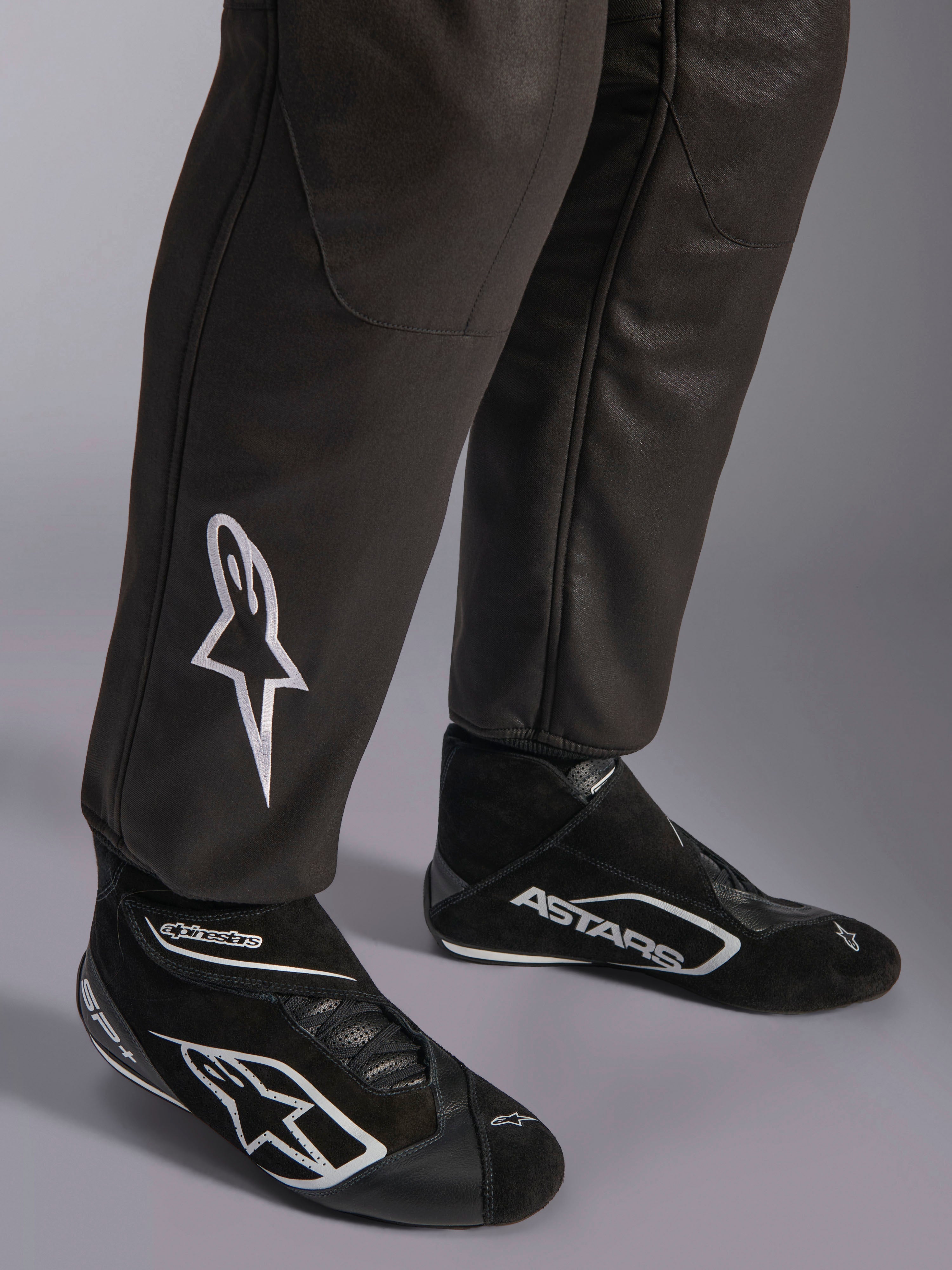 Combinaison Alpinestars GP Race V3 FIA, gros plan sur le bas des jambes et les bottines de course, noir avec accents argentés, arborant un logo étoile blanc brodé sur le tibia et des poignets de cheville côtelés, équipement de protection professionnel pour la course automobile