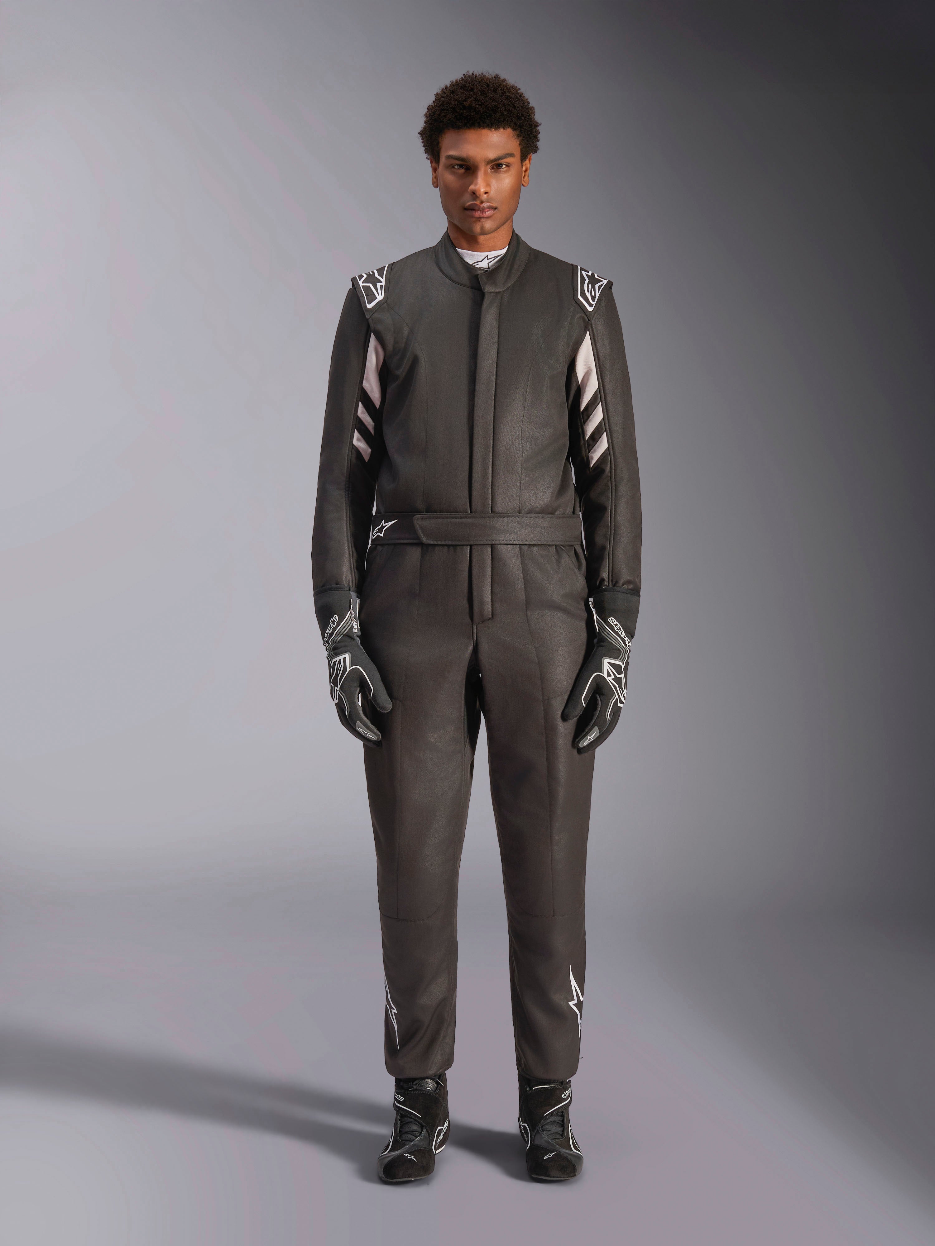 Alpinestars GP Race V3 Suit FIA, combinaison de course automobile, noir et argent, vue de face d'un pilote portant un équipement de course complet incluant gants et bottines, design professionnel de sport automobile avec logos Alpinestars sur les épaules et la ceinture