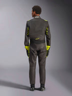 Alpinestars GP Race V3 Pak FIA, achteraanzicht, zwart met Yellow Fluo accenten, voorzien van gele panelen op de armen en de romp, geel logo op de onderrug, gedragen met bijpassende racehandschoenen en -laarzen, professioneel autoracepak.