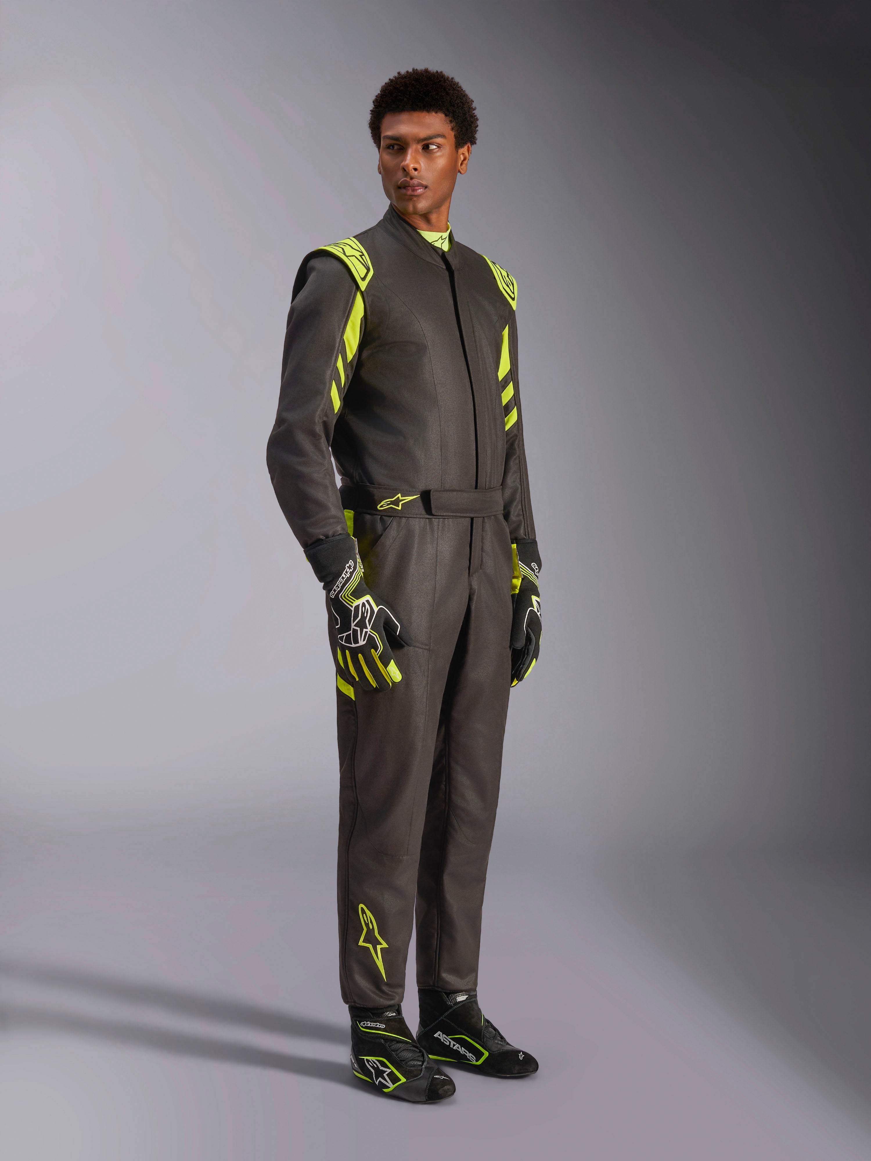 Alpinestars GP Race V3 Suit FIA, autoracepak, zwart met fluoriserend geel, gedragen door een model met bijpassende racehandschoenen en laarzen, voorzien van opvallende gele accenten op de schouders en benen, professionele motorsportuitrusting