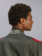 Alpinestars GP Race V3 Suit FIA, combinaison de course rouge anthracite, gros plan sur le col arrière montrant l'étiquette de certification FIA 8856-2018 et les épaulettes rouges, vue détaillée d'un équipement de sport automobile professionnel.
