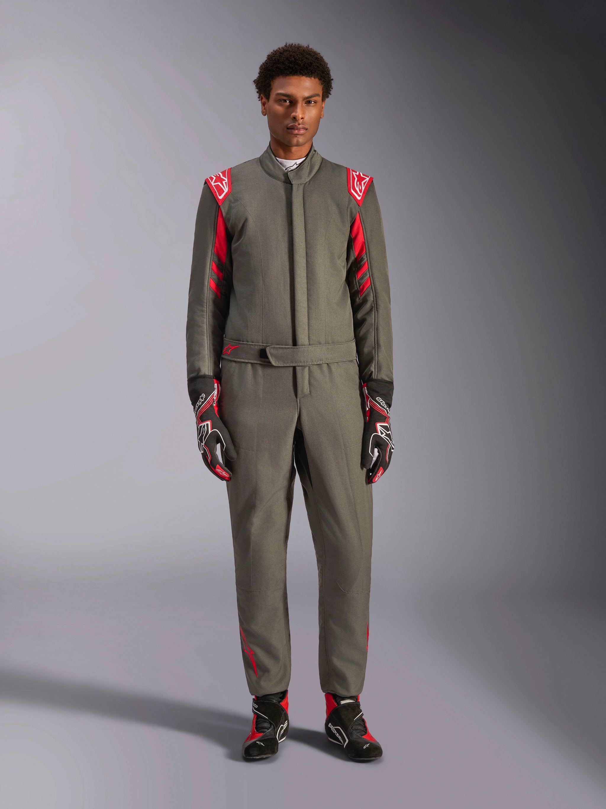 Alpinestars GP Race V3 Suit FIA, combinaison de course automobile, anthracite et rouge, portée par un mannequin homme avec gants et bottines assortis, avec épaulettes rouges et logos de la marque, équipement de sport automobile professionnel pour la conduite de performance