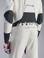Combinaison Alpinestars Hypertech V3, combinaison de course automobile blanc, noir et argent, vue arrière montrant le grand logo 'alpinestars' noir et le texte 'RACING AHEAD', avec des panneaux extensibles noirs aux coudes et aux lombaires, vêtement de protection professionnel pour le sport automobile.