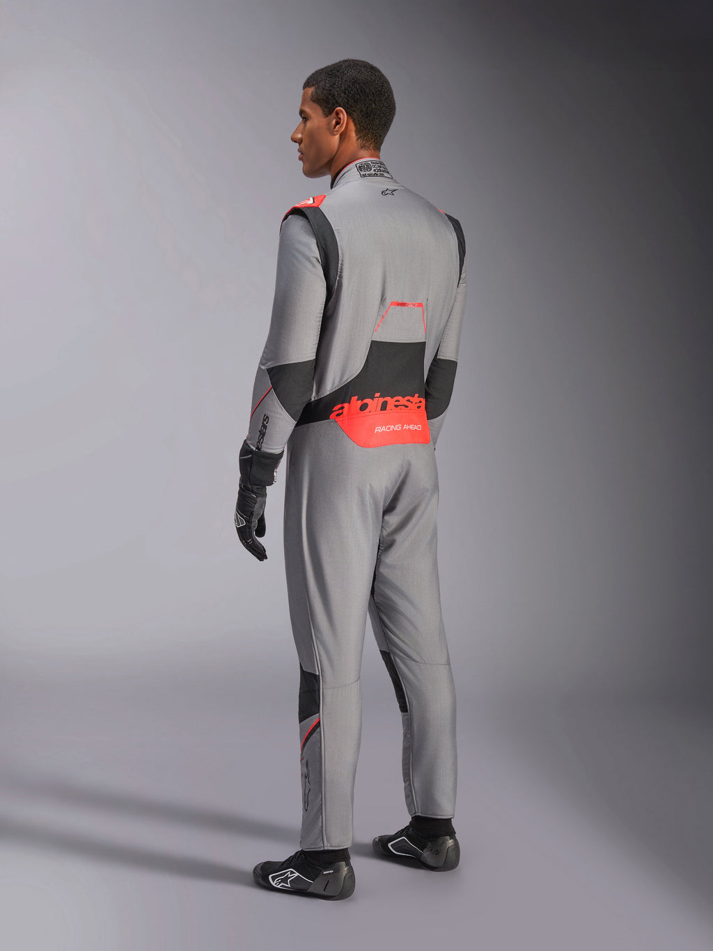 Alpinestars Hypertech V3 Suit in Mid Gray Black Red Fluo, driekwart achteraanzicht, met opvallende rode Alpinestars-branding op de onderrug, zwarte stretchpanelen en een slanke atletische pasvorm voor professionele autoraces.