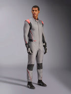 Mannelijk model draagt het Alpinestars Hypertech V3-pak in Mid Gray met zwarte en Red Fluo accenten, professioneel autoracepak gecombineerd met zwarte racehandschoenen en schoenen, voorzien van een lichtgewicht tweelaagse Nomex-constructie met rode schouderdetails en een atletische pasvorm.