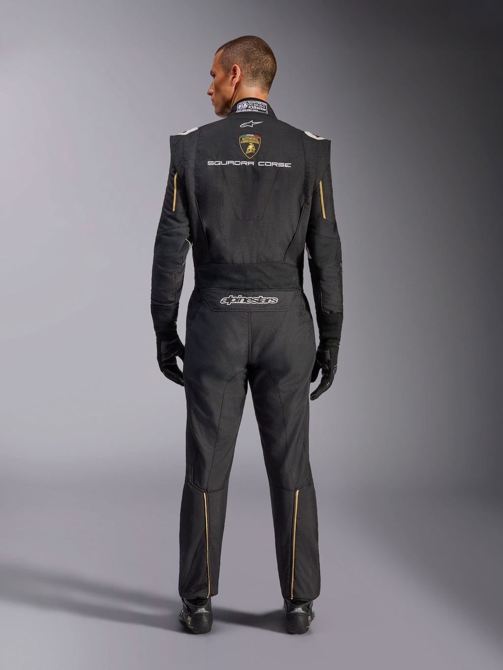 Combinaison Alpinestars Édition Limitée Lamborghini GP Tech V4 FIA, combinaison de course automobile, noire avec accents dorés et argentés, vue arrière montrant le logo Lamborghini Squadra Corse, le logo Alpinestars et des liserés dorés sur les manches et les jambes, équipement de course professionnel