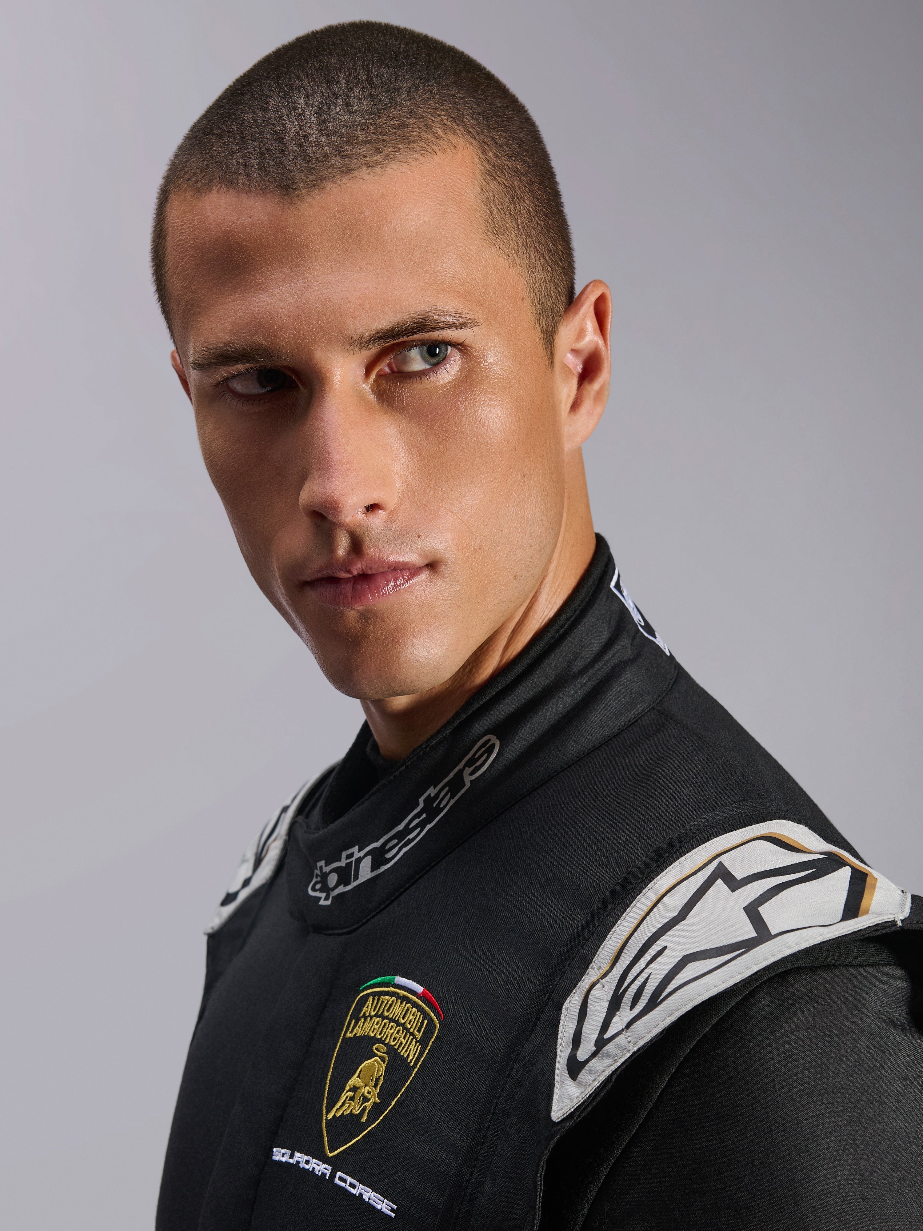 Gros-plan d'un mannequin portant la combinaison Lamborghini GP Tech V4 Édition Limitée, noir, argent et or, avec les logos Automobili Lamborghini Squadra Corse et Alpinestars, équipement de course automobile professionnel certifié FIA