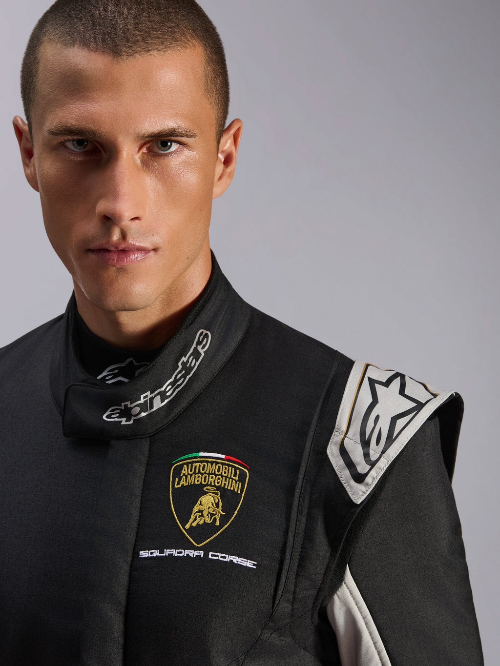 Alpinestars Limited Edition Lamborghini GP Tech V4 Suit, combinaison de course professionnelle, noire avec accents argent et or, gros-plan présentant le logo Lamborghini Squadra Corse sur la poitrine et le marquage Alpinestars au col, protection haut de gamme pour le sport automobile