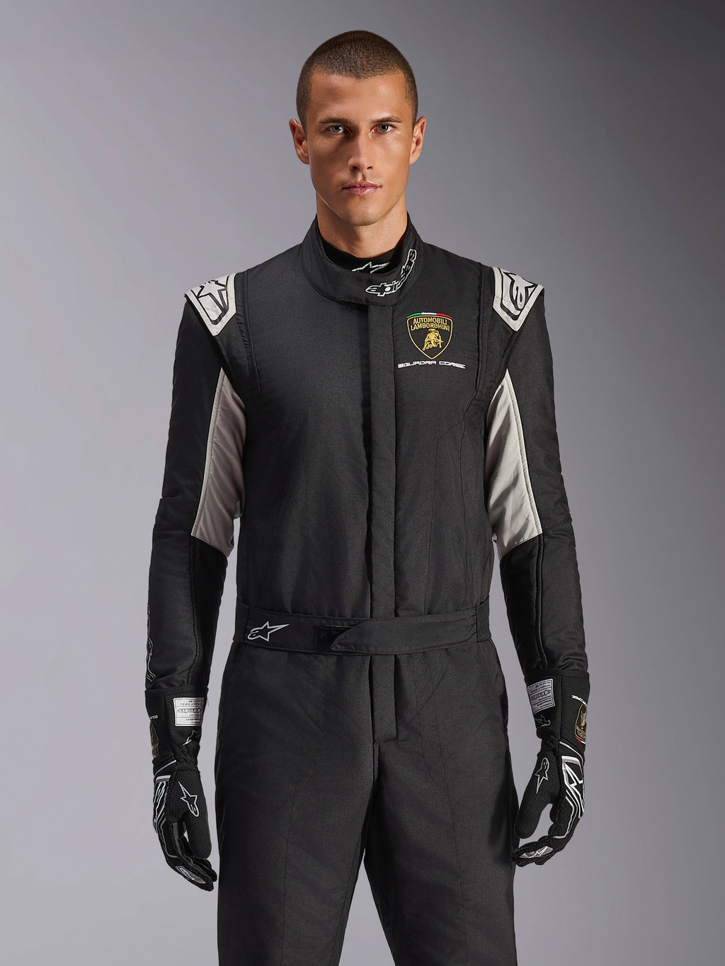 Combinaison Alpinestars GP Tech V4 Édition Limitée Lamborghini, combinaison de course professionnelle noire avec accents argentés et dorés, arborant l'écusson Automobili Lamborghini Squadra Corse sur la poitrine, portée par un mannequin avec des gants de course noirs assortis.