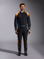 Combinaison Alpinestars GP Pro Comp V2 FIA, combinaison de course automobile noir asphalte et orange fluo, mannequin portant un équipement de protection complet avec gants et chaussures de course assortis, logos Alpinestars blancs et panneaux latéraux orange vif, vêtement de sport automobile professionnel