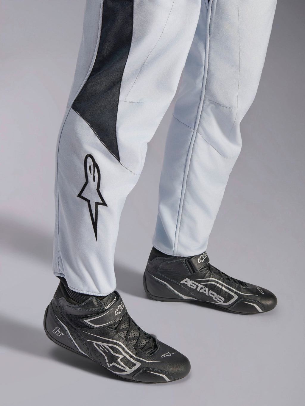 Alpinestars GP Pro Comp V2 FIA, combinaison de course auto grise et noire, bas des jambes avec logo et bottines de racing.