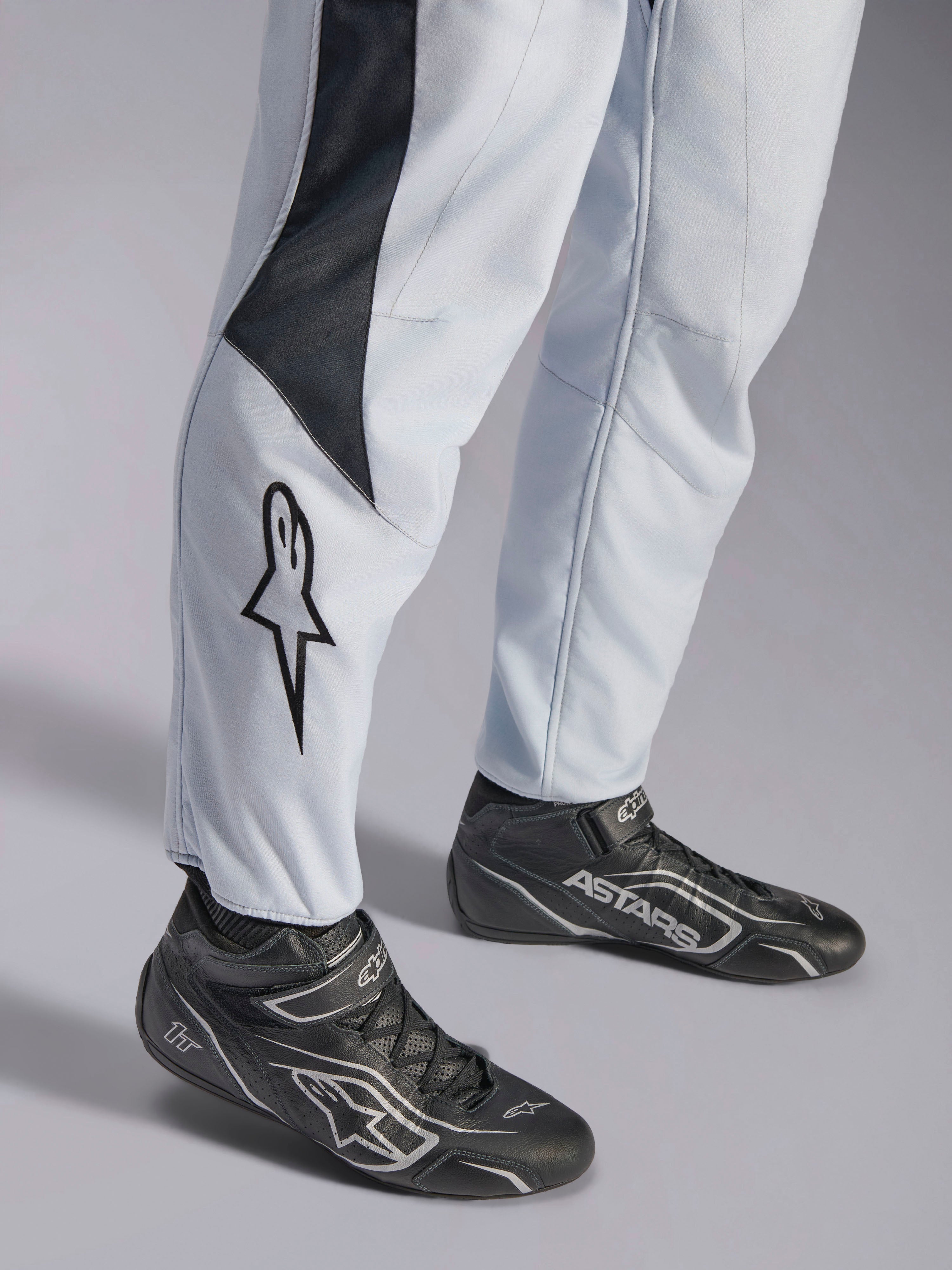 Alpinestars GP Pro Comp V2 FIA, combinaison de course auto grise et noire, bas des jambes avec logo et bottines de racing.