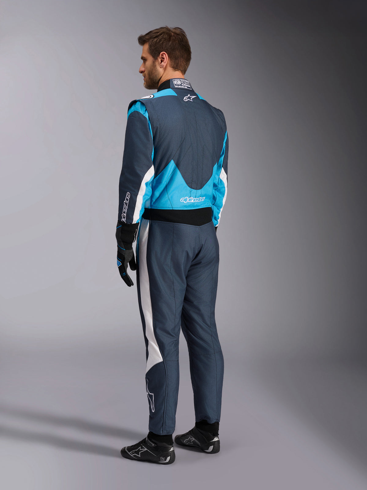 Alpinestars GP Pro Comp V2 FIA pak, donkergrijs en cyaanblauw autoracepak, achteraanzicht gedragen door een model.