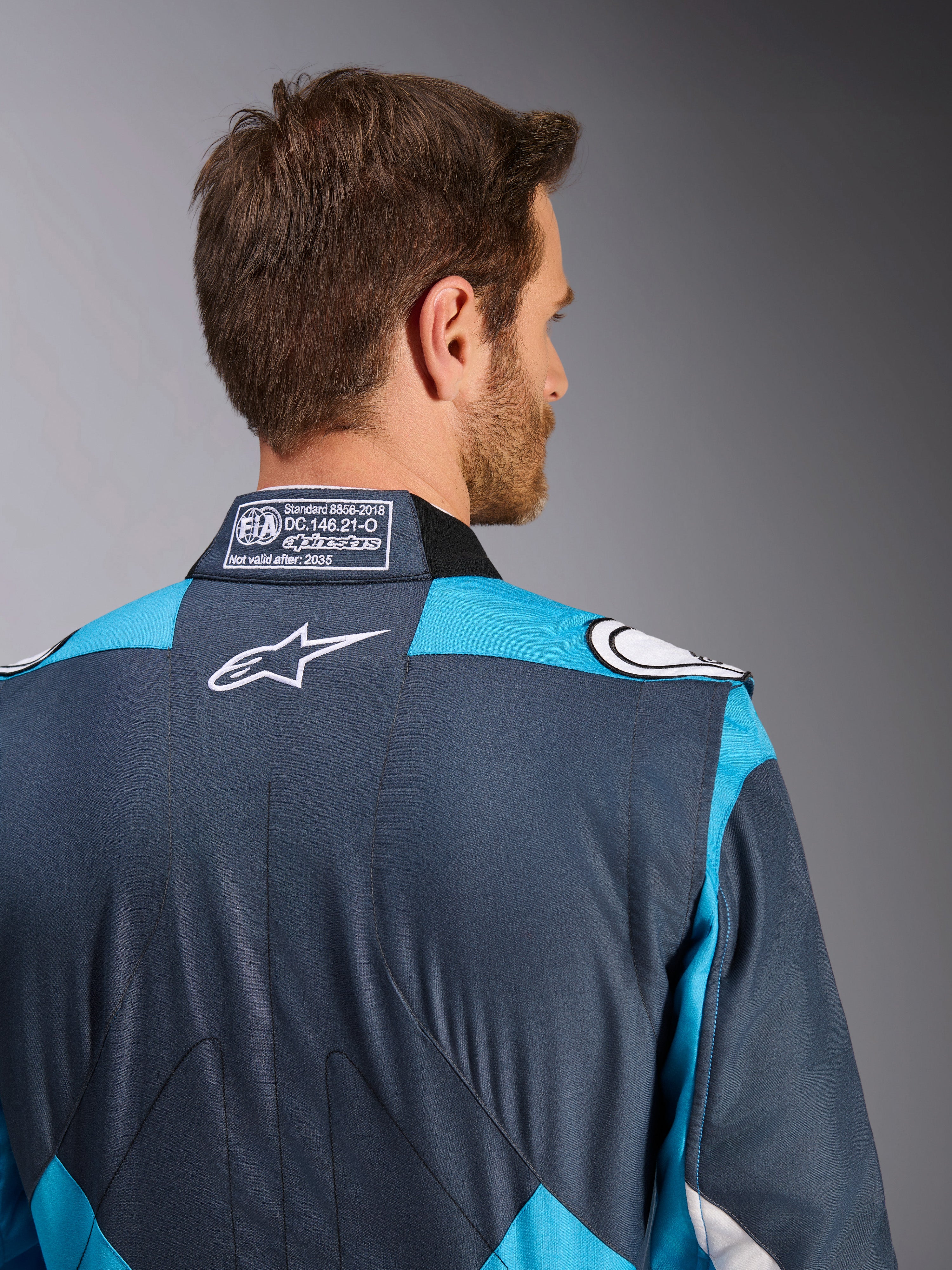 Alpinestars GP Pro Comp V2 FIA, combinaison de course automobile pour homme, bleu cyan et gris asphalte, logo blanc et étiquette FIA sur le col.