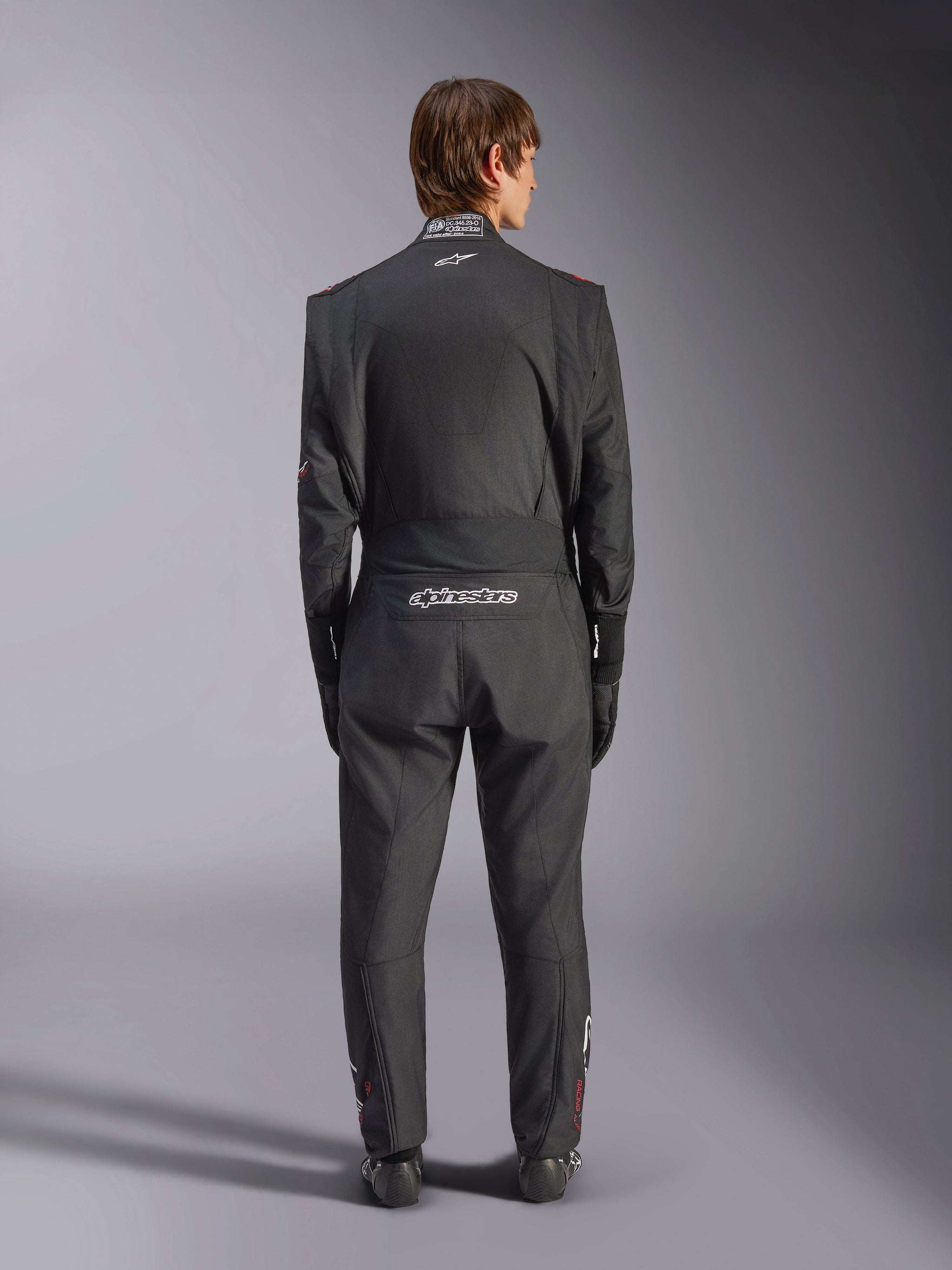 Alpinestars GP Tech V4 Suit, combinaison de sport automobile, noir et blanc, vue arrière présentant le logo Alpinestars blanc et l'homologation FIA sur le col, coupe ergonomique pour la protection des pilotes professionnels