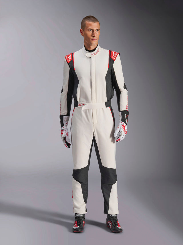 Combinaison Alpinestars GP Tech V4, combinaison de course automobile une pièce, blanc, noir et rouge, portée par un mannequin homme avec gants et chaussures de course assortis, avec logos rouges sur les épaules et panneaux latéraux noirs, équipement professionnel de sport automobile pour circuit