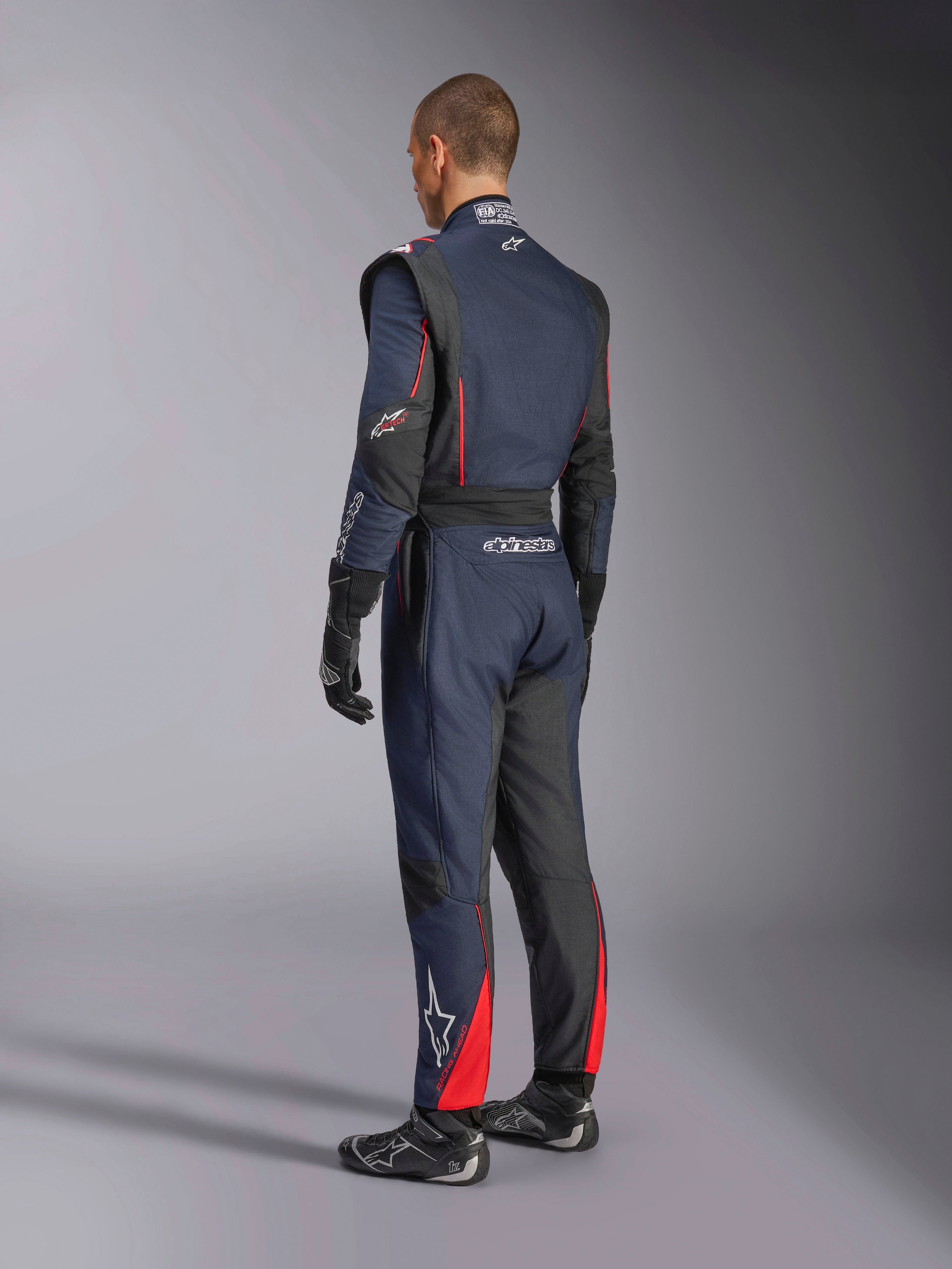 Alpinestars GP Tech V4 Pak, navyblauw zwart rood, achteraanzicht van professioneel eendelig autoracepak met rode accenten en zwarte panelen, gedragen met zwarte racehandschoenen en schoenen, FIA-gecertificeerde motorsportuitrusting