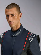 Close-up portret van een model dat het Alpinestars GP Tech V4 Suit draagt, een autoracepak in Blue Navy, zwart en rood, met Alpinestars-branding op de hoge kraag en gestructureerde schouderepauletten.