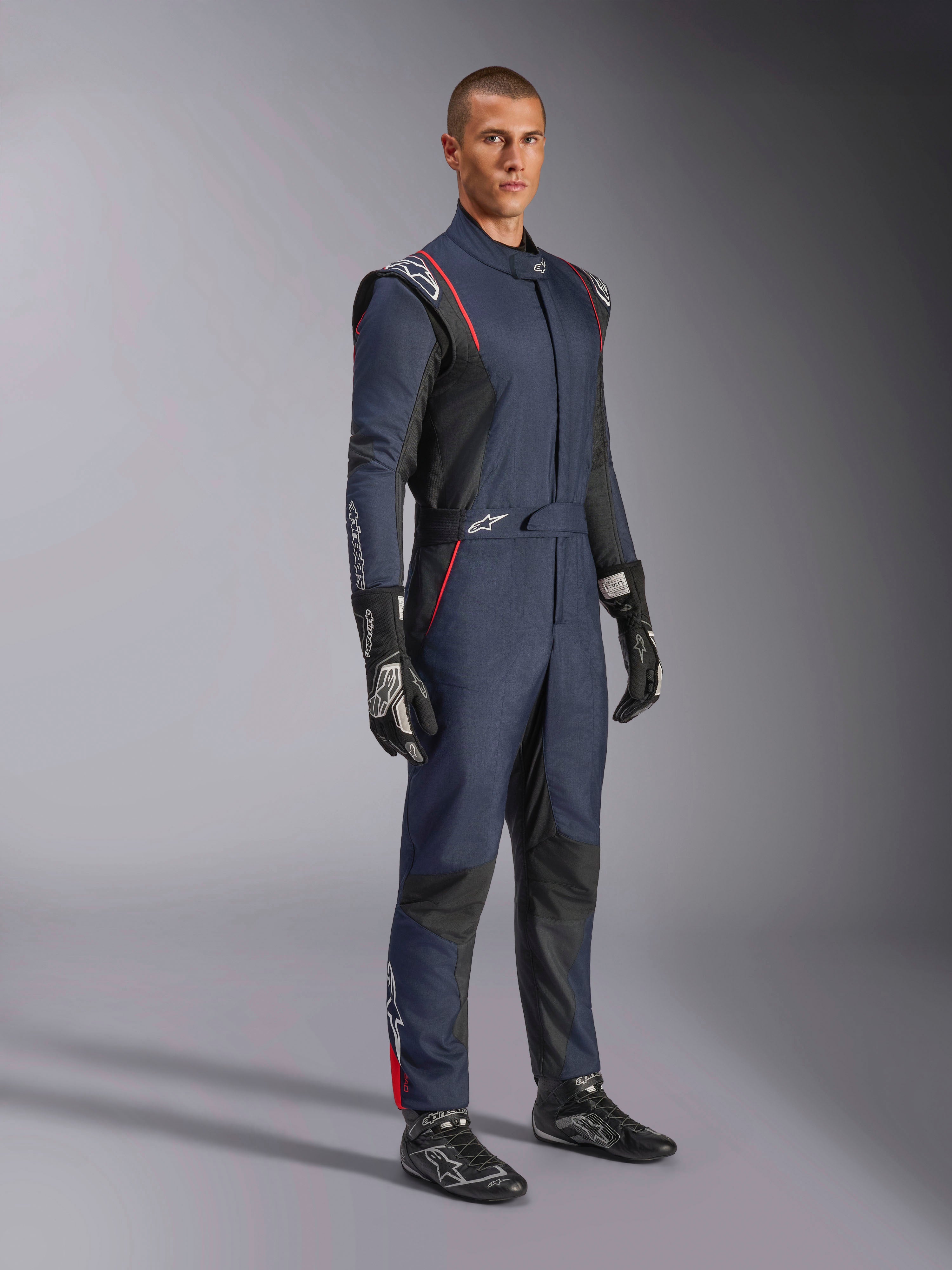 Alpinestars GP Tech V4 Suit, eendelig autoracepak, navyblauw, zwart en rood, gedragen door een model met zwarte racehandschoenen en laarzen, voorzien van zwarte panelen en rode biezen, professionele motorsportuitrusting.