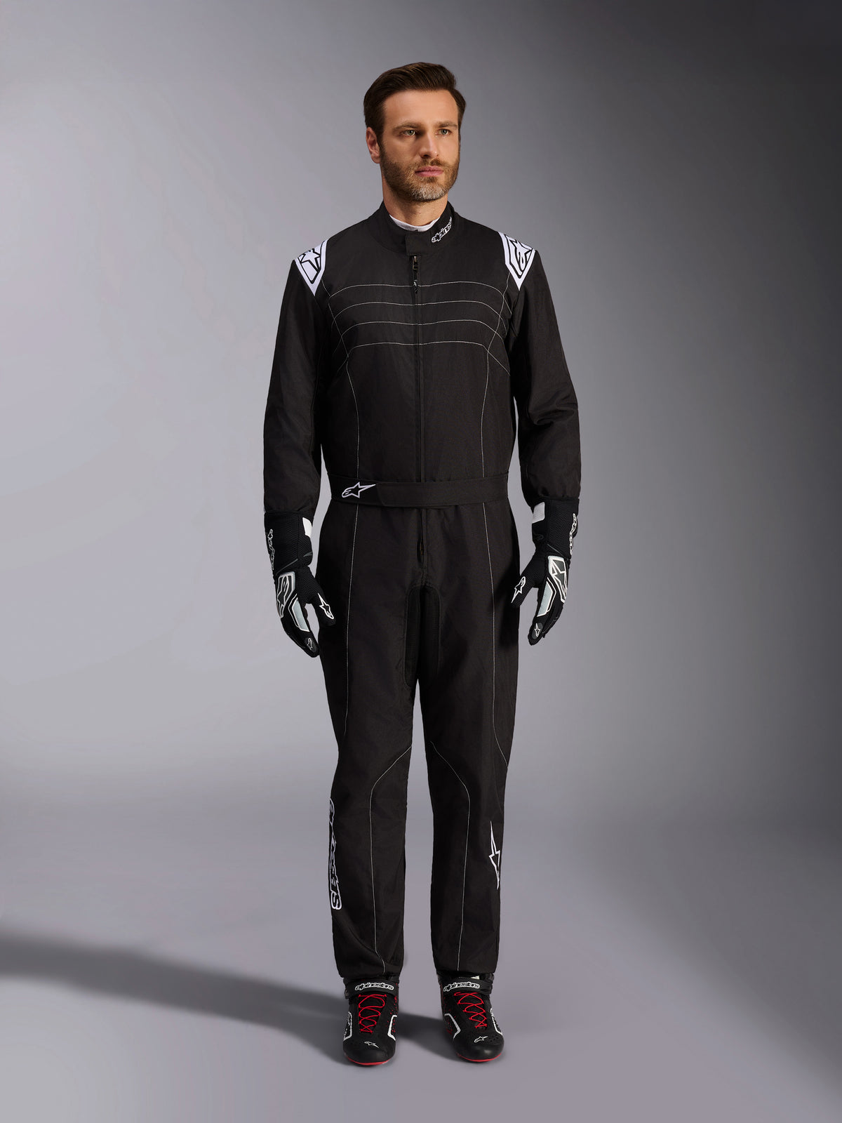 Alpinestars KMX-9 V3 Anzug, schwarz-weißer Kart-Anzug, Ganzkörperansicht an einem Modell, mit weißen Schulterlogos und Akzenten, kombiniert mit schwarz-weißen Rennhandschuhen und schwarzen Schuhen mit roten Schnürsenkeln, sportlich-reguläre Passform für professionelle Kart-Ausrüstung.