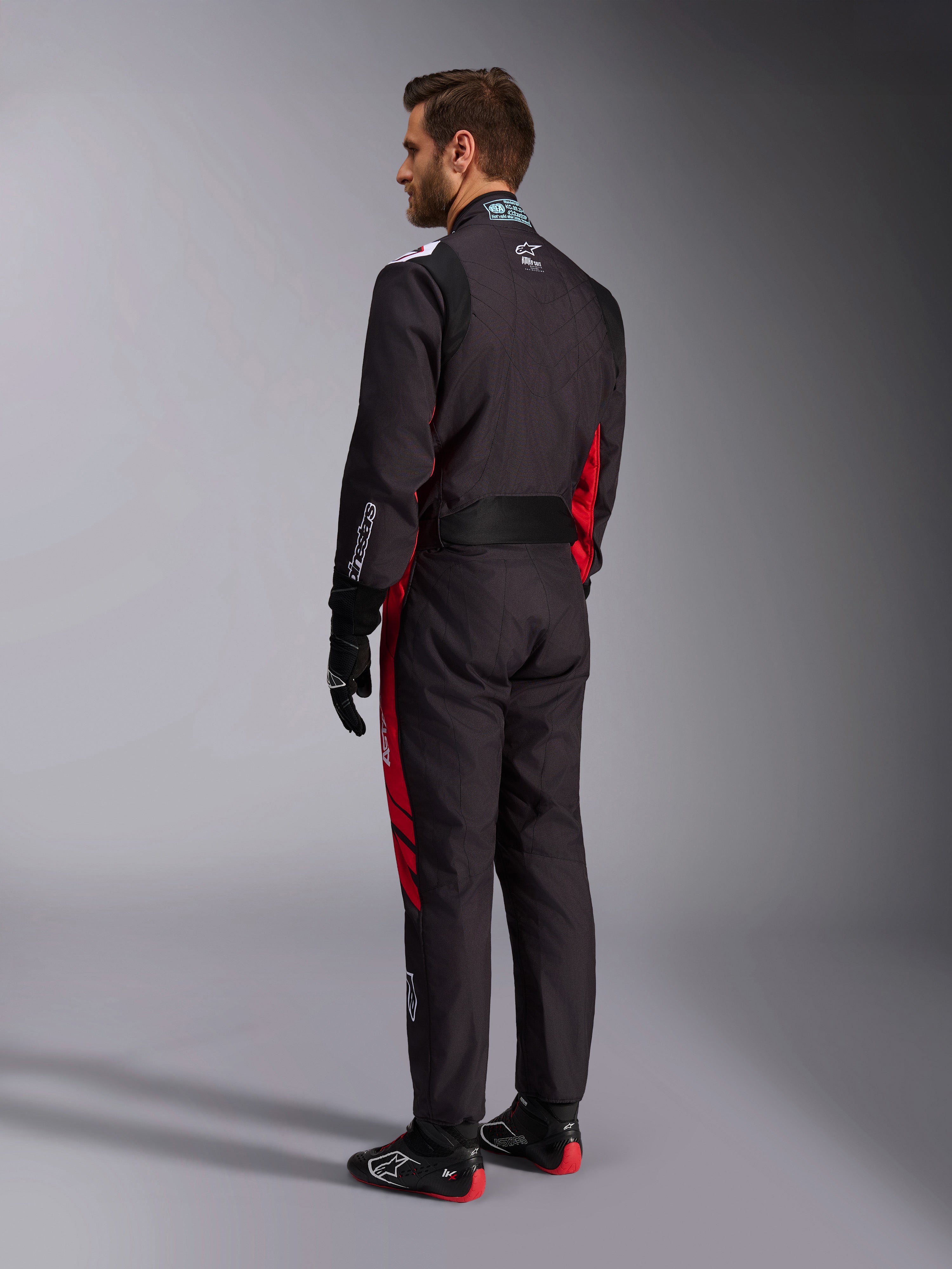 Alpinestars KMX-9 V3 Graphic 3 Suit, Black and Red, back view of model wearing full karting gear including black gloves and racing boots, featuring red side panels and white logo details