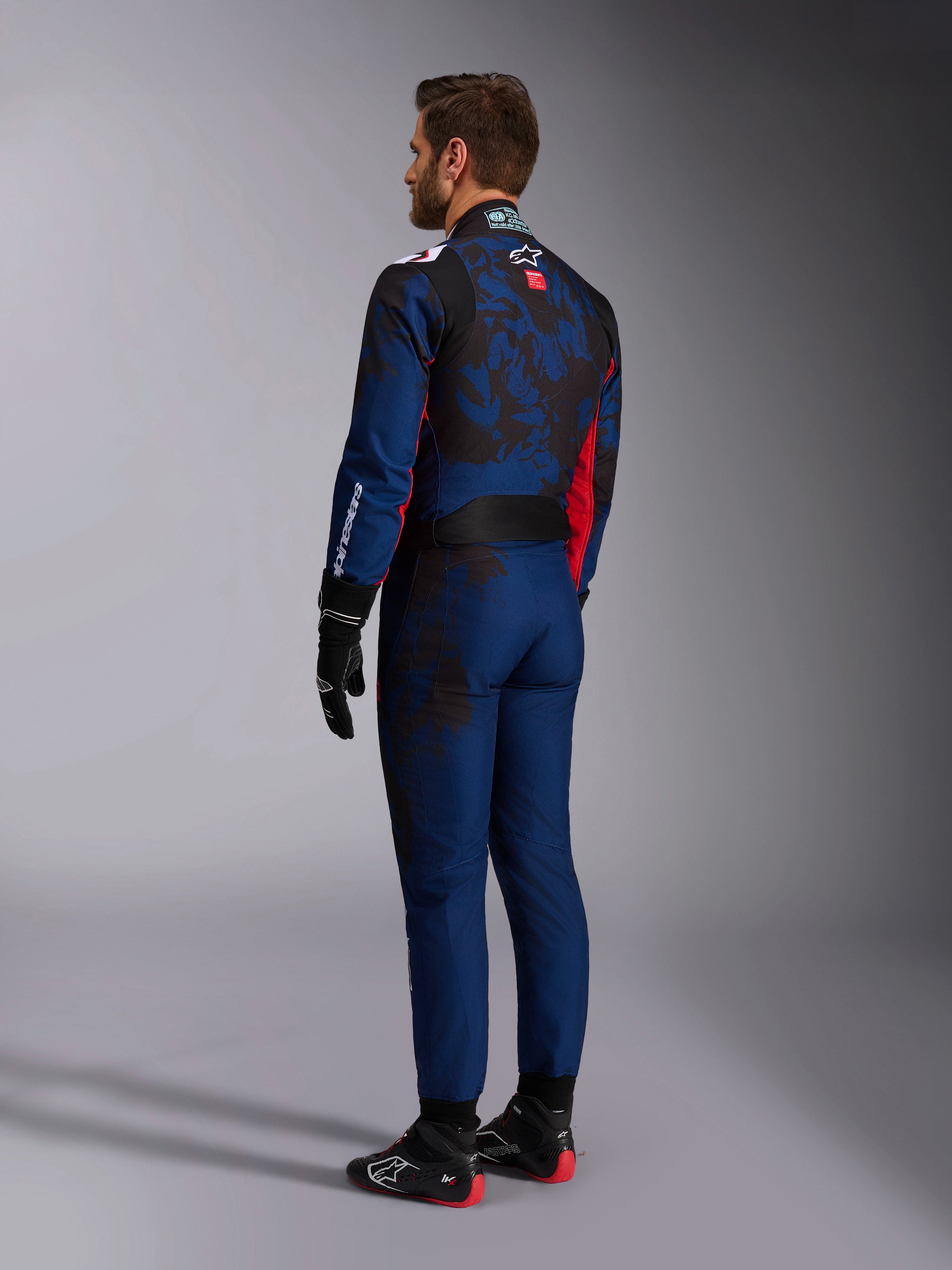 Alpinestars KMX-9 V3 Graphic 5 Suit, Karting Suit, Navy Red, rear view showing a navy blue body with a dark camo-inspired graphic on the back and red accents, worn with black racing gloves and black and red karting shoes.