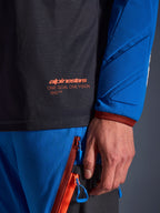 Nahaufnahme des Alpinestars Maxdura Dual Jersey in Deep Gray und Royal Blue, mit orangefarbenem Logo und 'One Goal One Vision' Schriftzug auf dem Mesh-Torso, gepolsterter Ärmel mit verstärkten geometrischen Einsätzen, technische Adventure-Fahrerausrüstung
