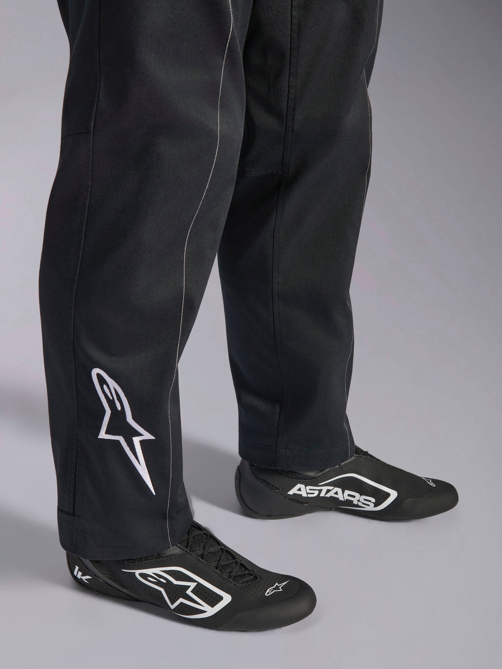 Alpinestars Kart Indoor V2 Suit, Black karting suit, close-up of lower legs and feet featuring a white Alpinestars logo on the calf, worn with matching black and white racing shoes, designed for recreational karting.