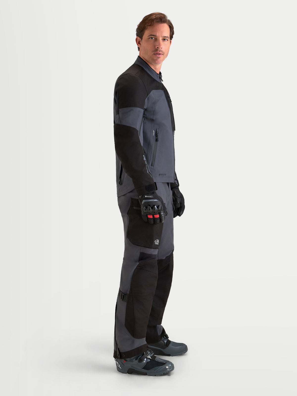 Alpinestars Arenis Gore-Tex Gear Set, adventure motorjas en motorbroek voor heren in zwart en donkergrijs, zijprofiel op model met bijpassende avontuurlijke uitrusting en waterdichte GORE-TEX constructie